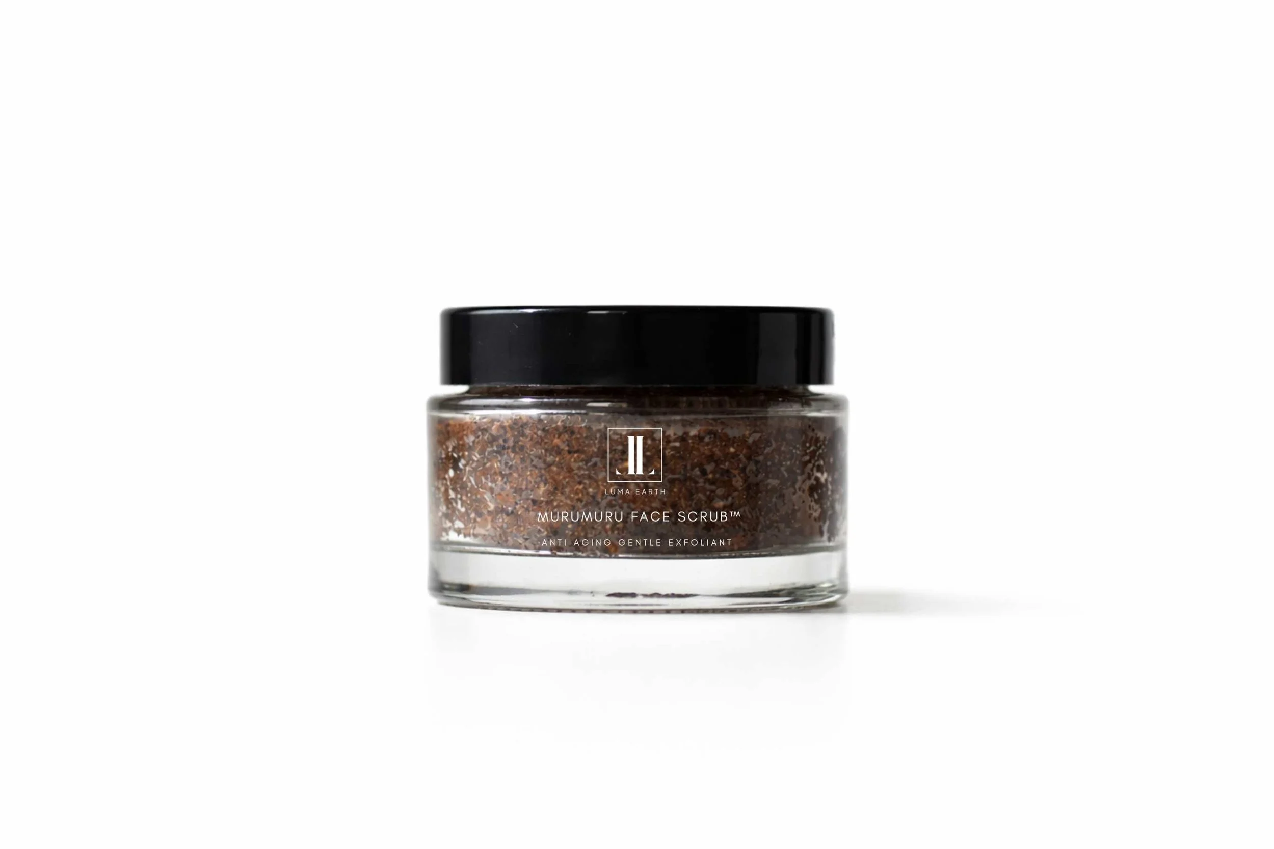 A clear glass jar of Luma Earth Murumuru Face Scrub with a black lid and brown exfoliating contents, placed on a white surface with a plain white background.
