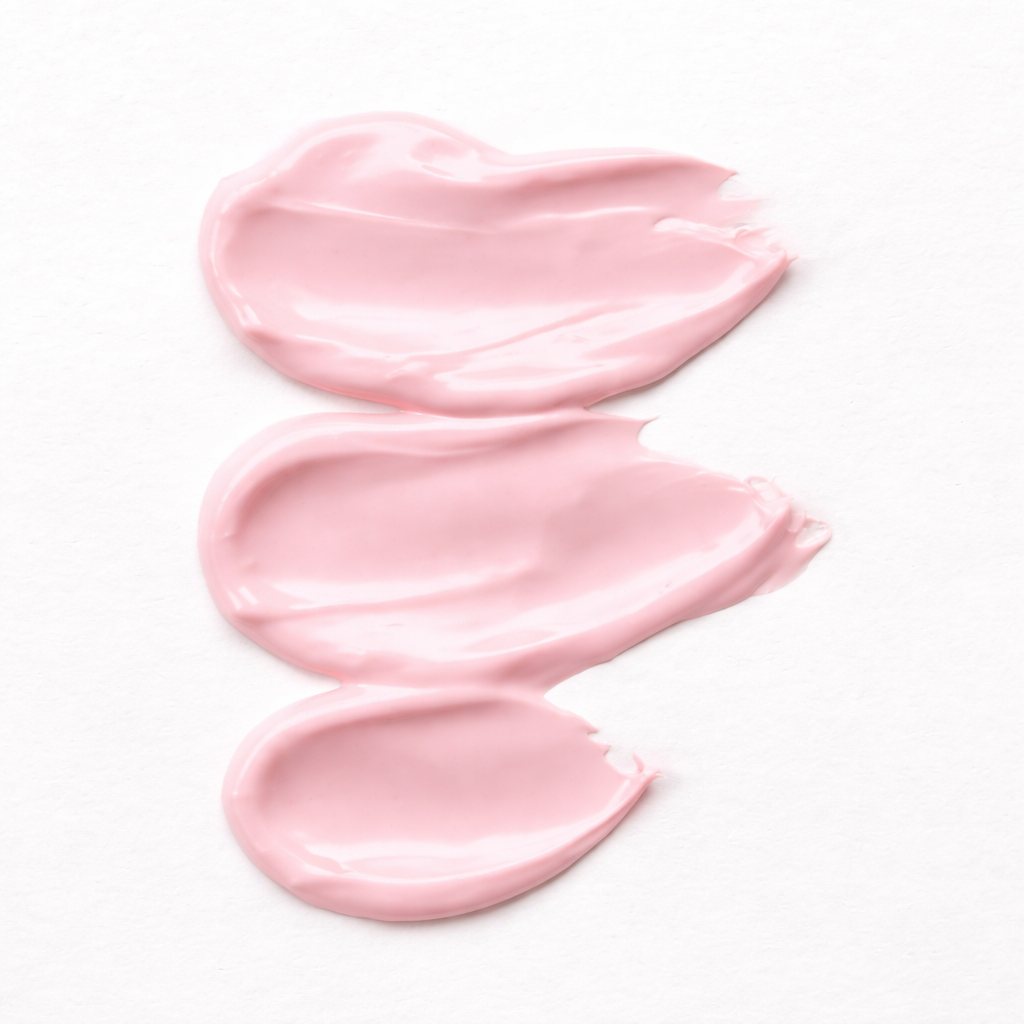 Three blobs of light pink cream or lotion spread on white surface.