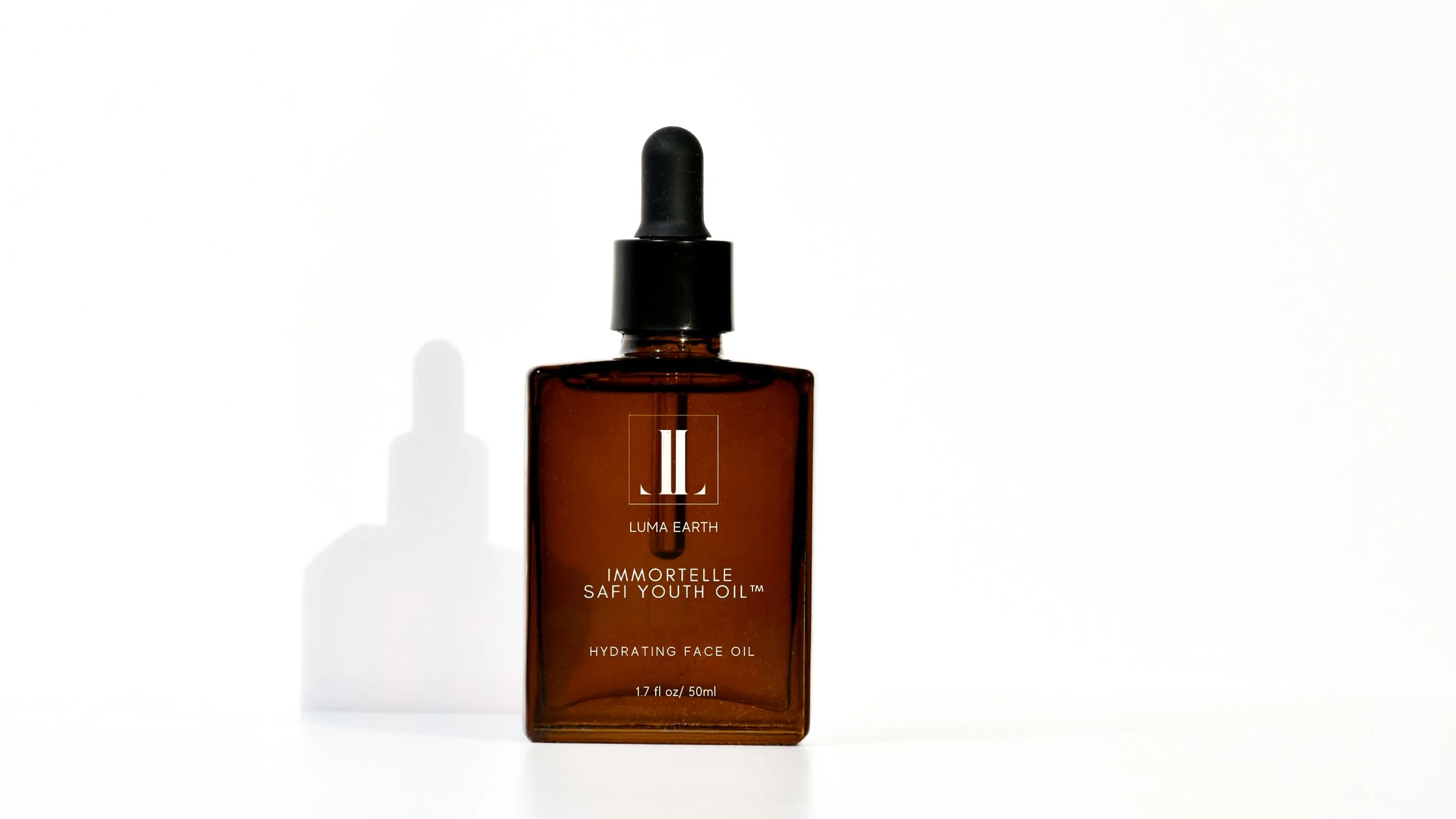 A brown glass bottle of Luma Earth Immortelle Safi Youth Oil, a hydrating face oil with a black dropper cap, casting a shadow on a white background.