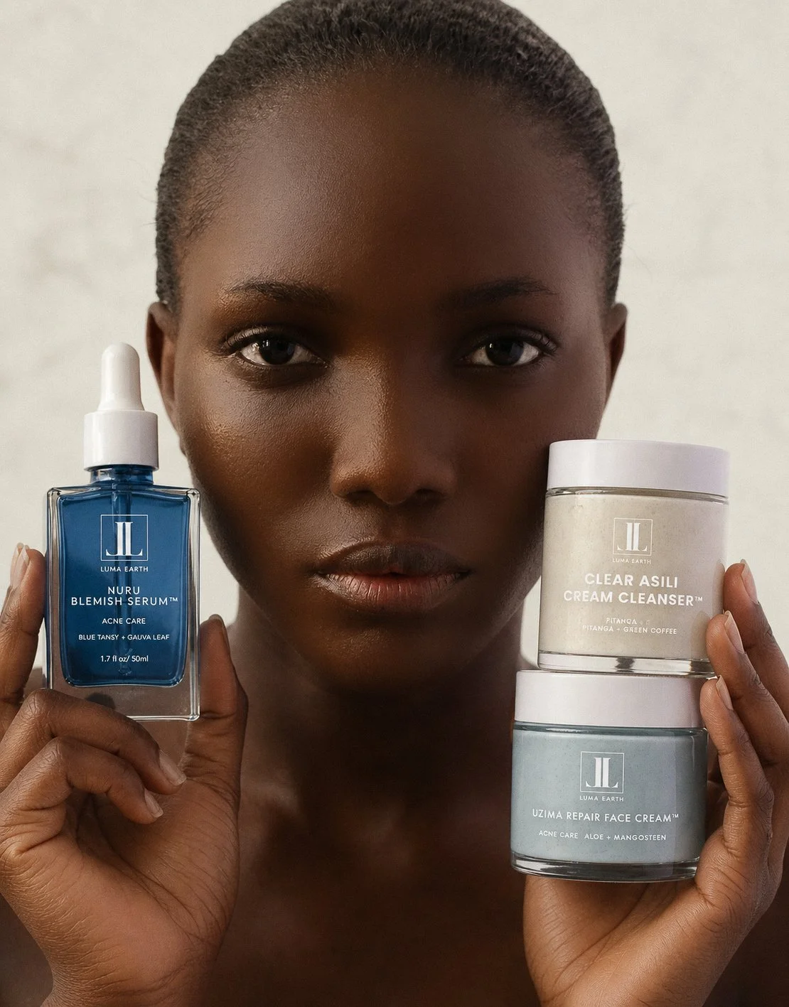 A woman holding skincare products, including a blue serum, a white cream cleanser, and a gray face cream from Luma Earth.