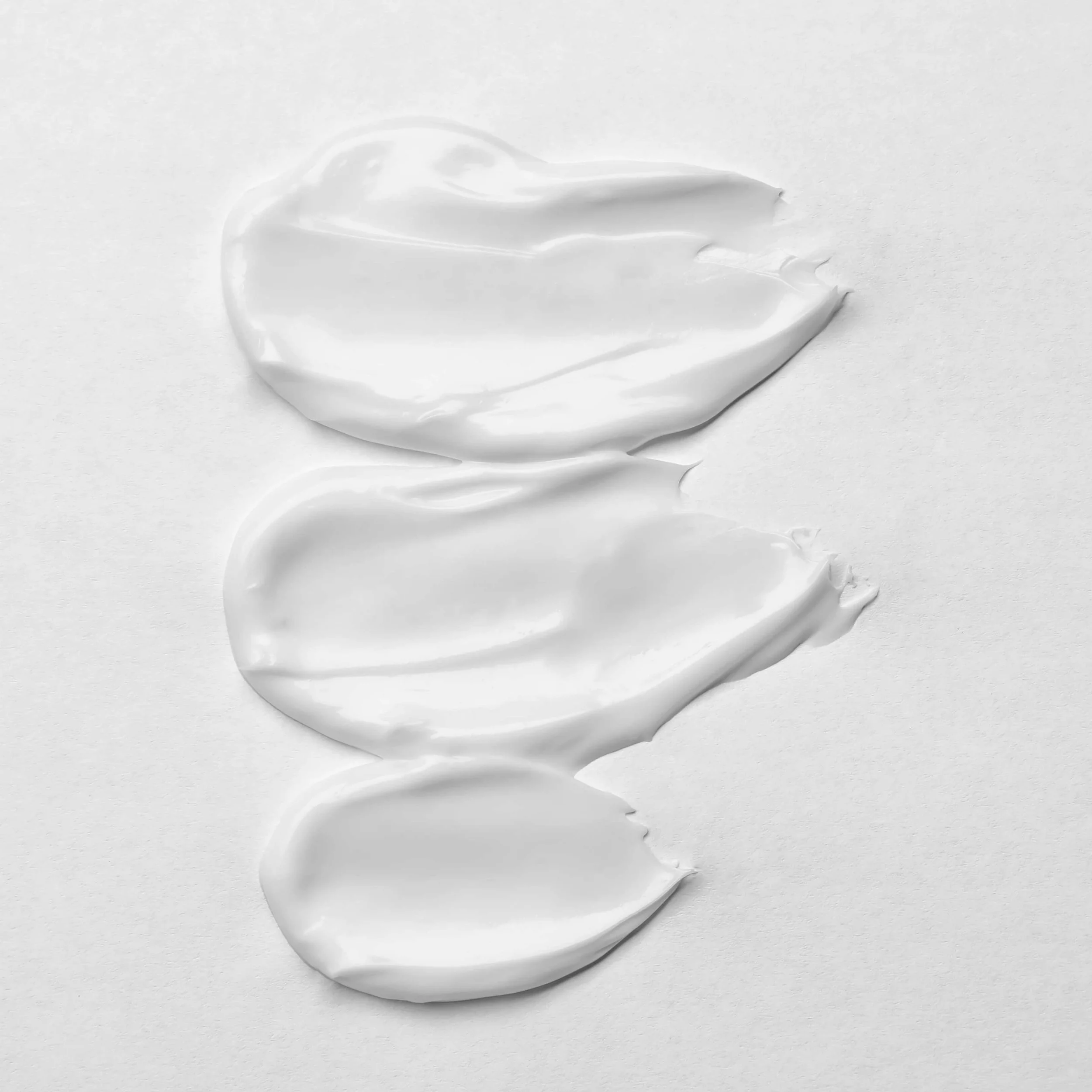 Three smears of white cosmetic cream on a white background.