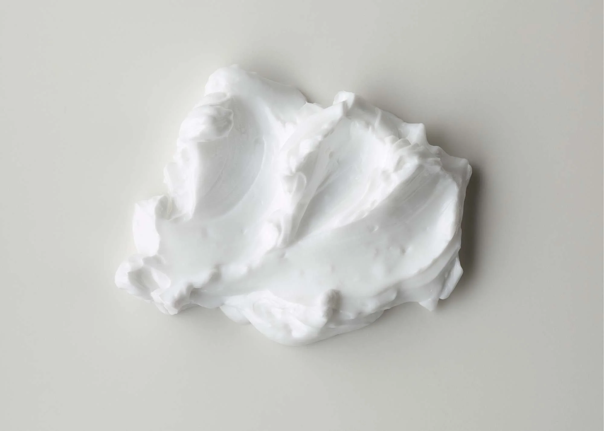 A dollop of white whipped face cream on a light surface.