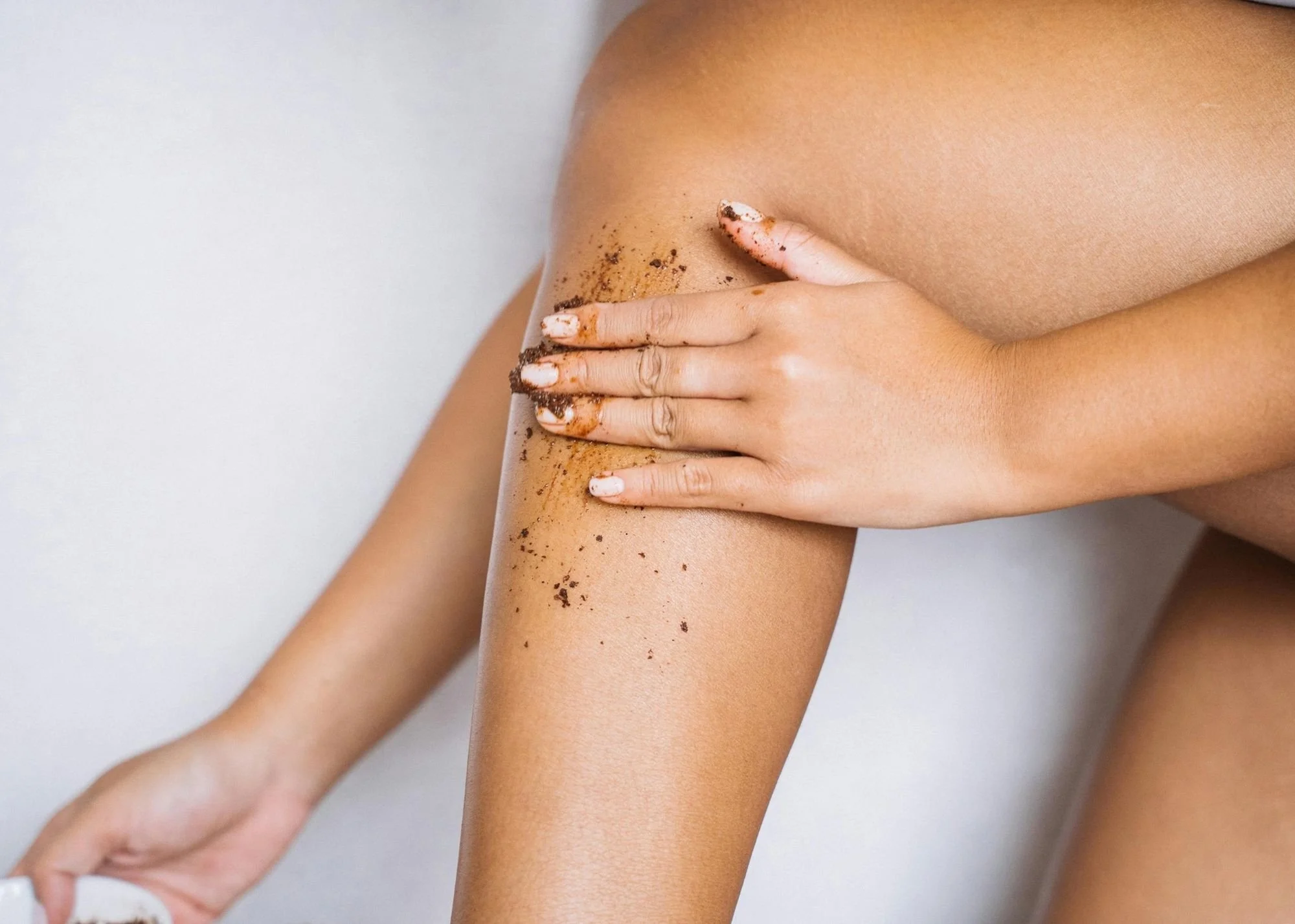 A person is applying coffee grounds to their leg, likely for a skincare or exfoliation treatment.