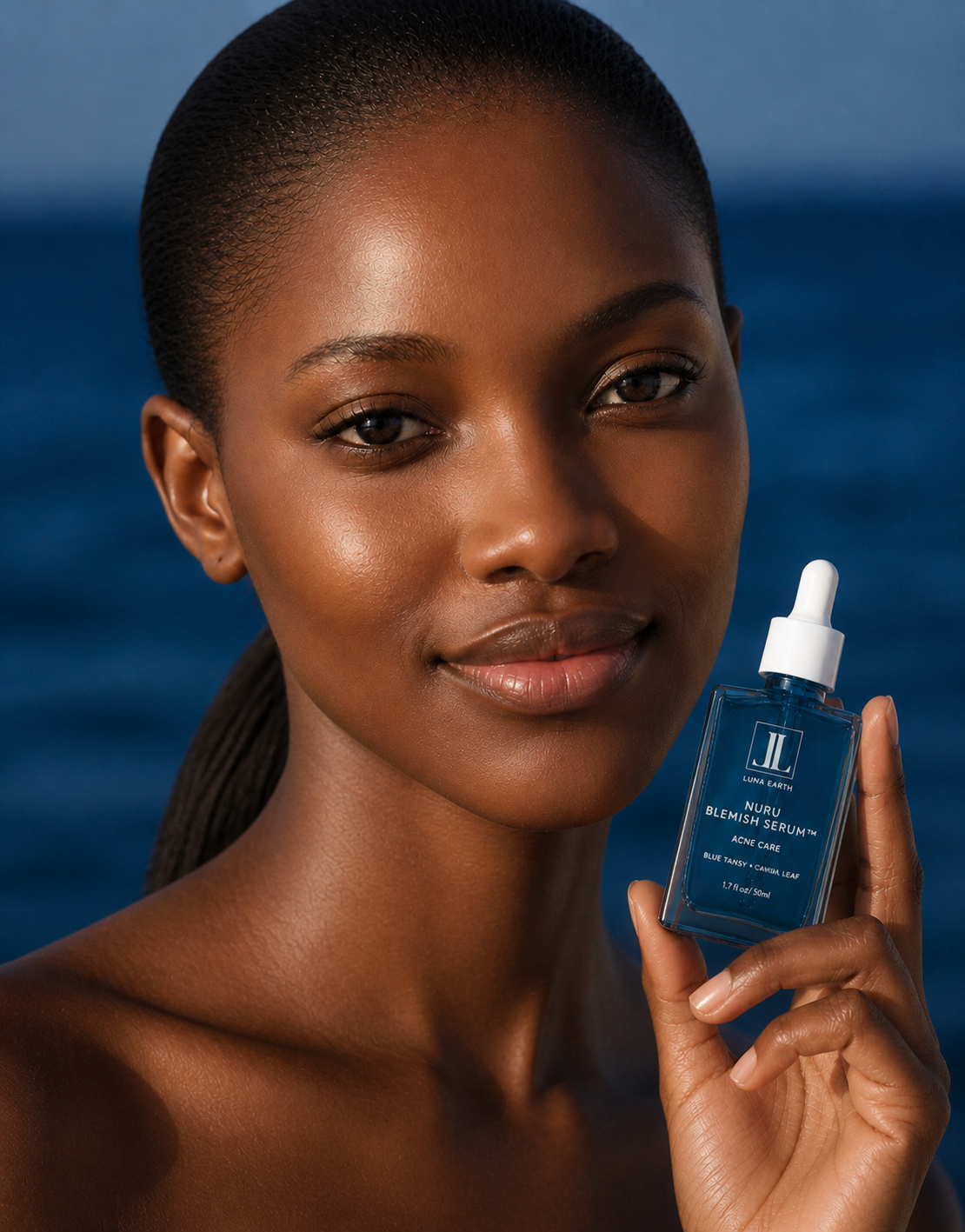 Close-up of a woman with dark skin holding a blue serum bottle labeled 'Nuru Blemish Serum' against a background of blue water, with a slight smile and smooth skin.