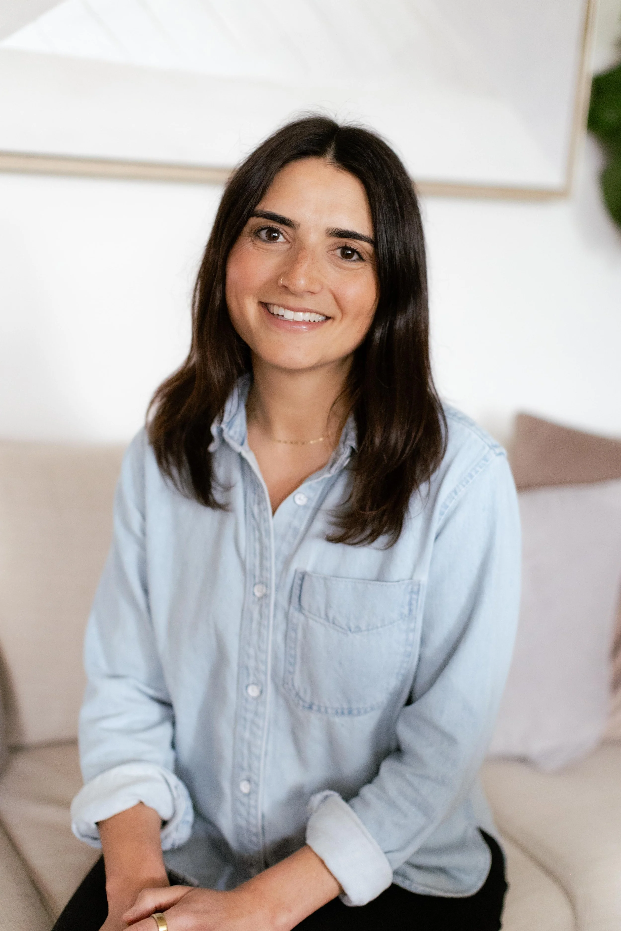 A woman with long dark hair and a light blue shirt smiling indoors.