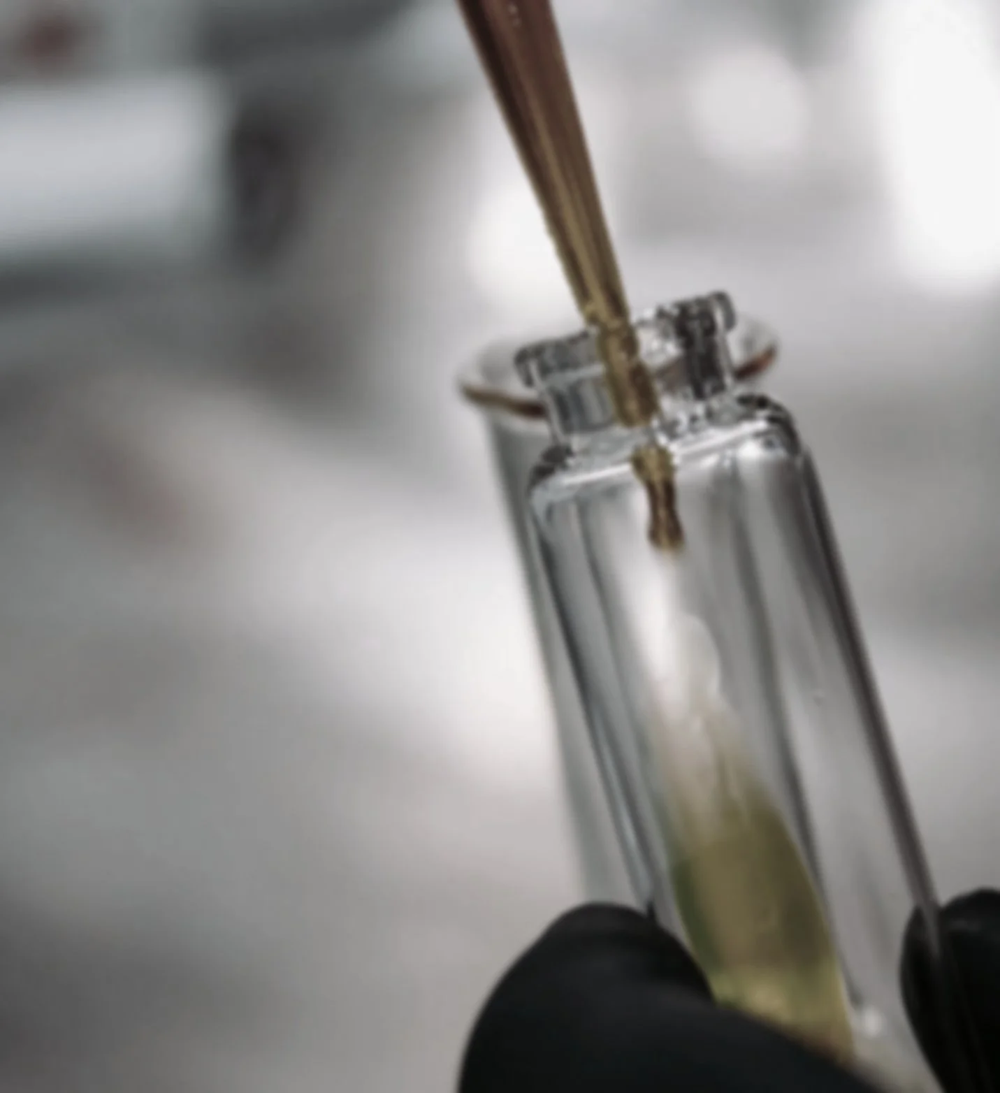 A glass test tube with a liquid inside, held by a gloved hand, and a pipette dispensing liquid into the test tube.