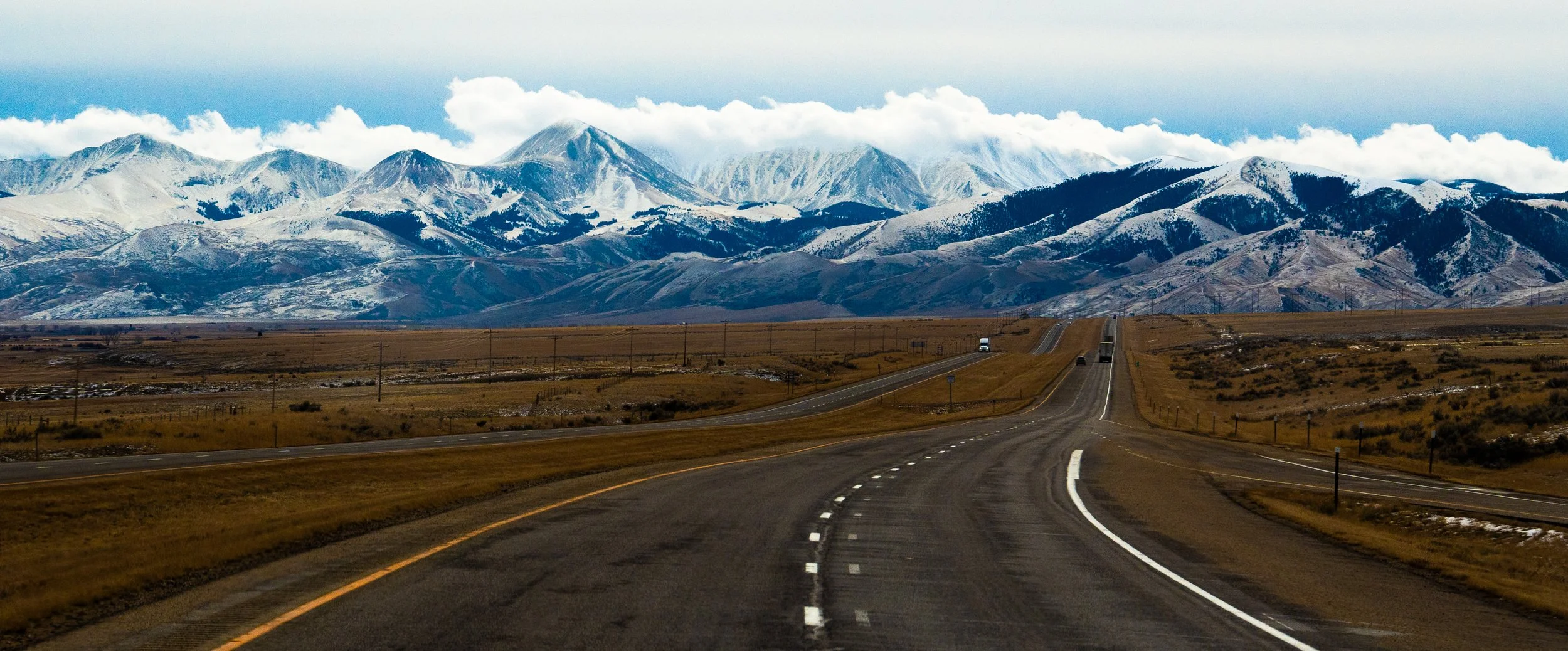 A winding highway leading towards snow-capped mountains under a partly cloudy sky.