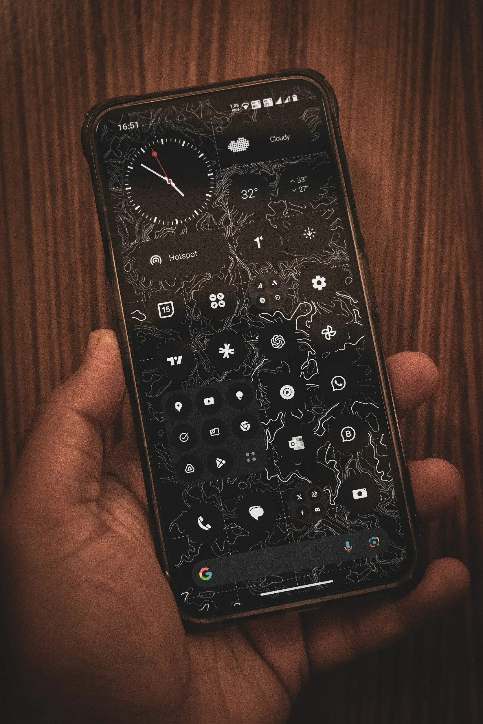 Close-up of a hand holding a smartphone displaying various app icons and widgets on a dark background.