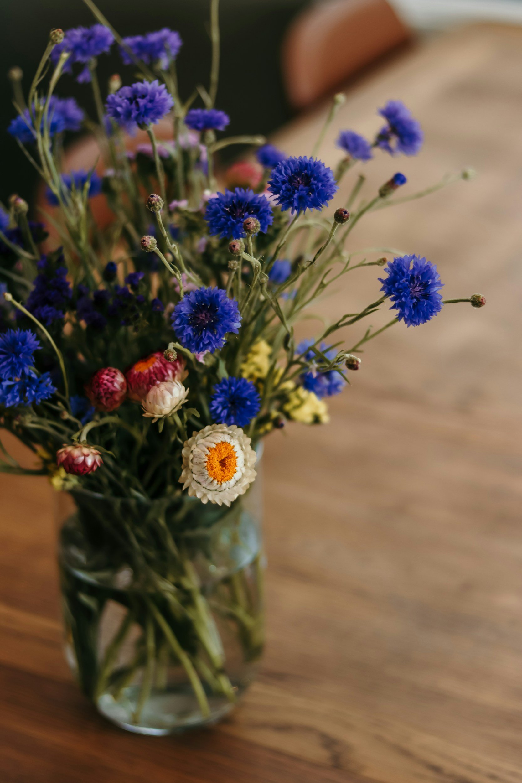 A glass jar filled with a bouquet of small blue, white, and pink flowers on a wooden table.