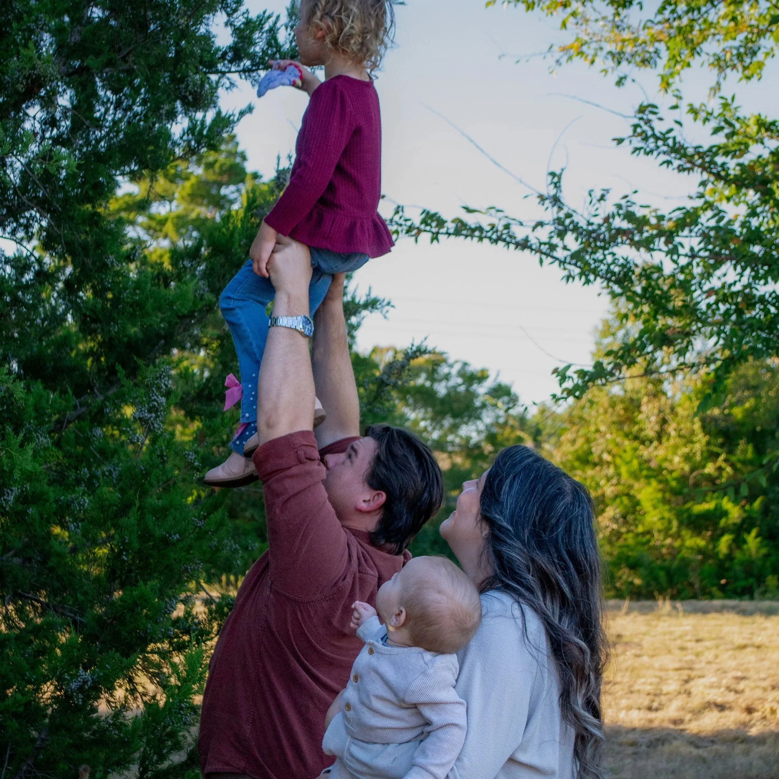 light of life birth doula's family in college station and bryan texas outdoors, with one child standing on another's shoulders, surrounded by green trees and sunlight.