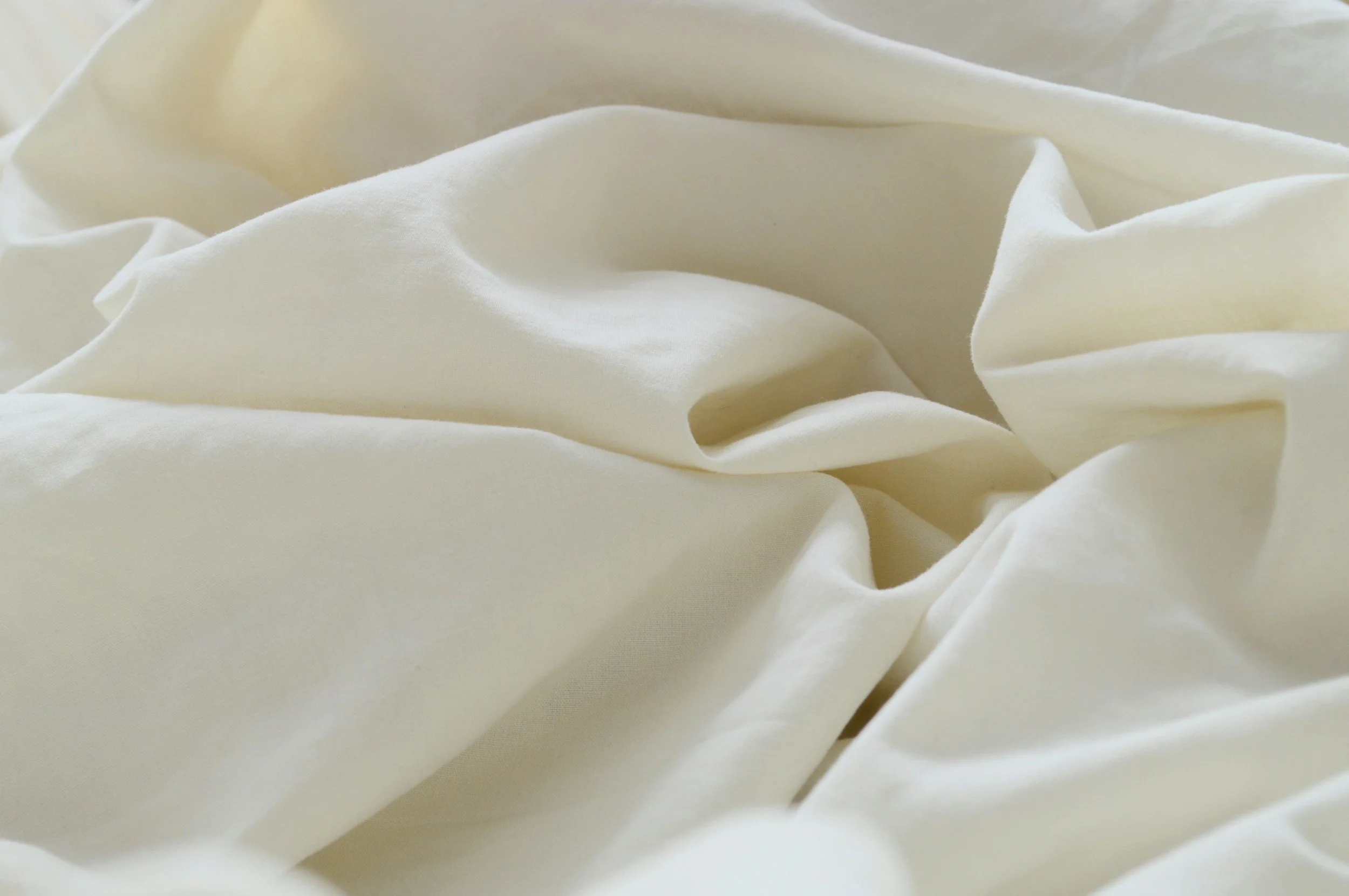 Close-up of cream-colored, soft, crumpled fabric with gentle folds and shadows to rest in during birth or postpartum.
