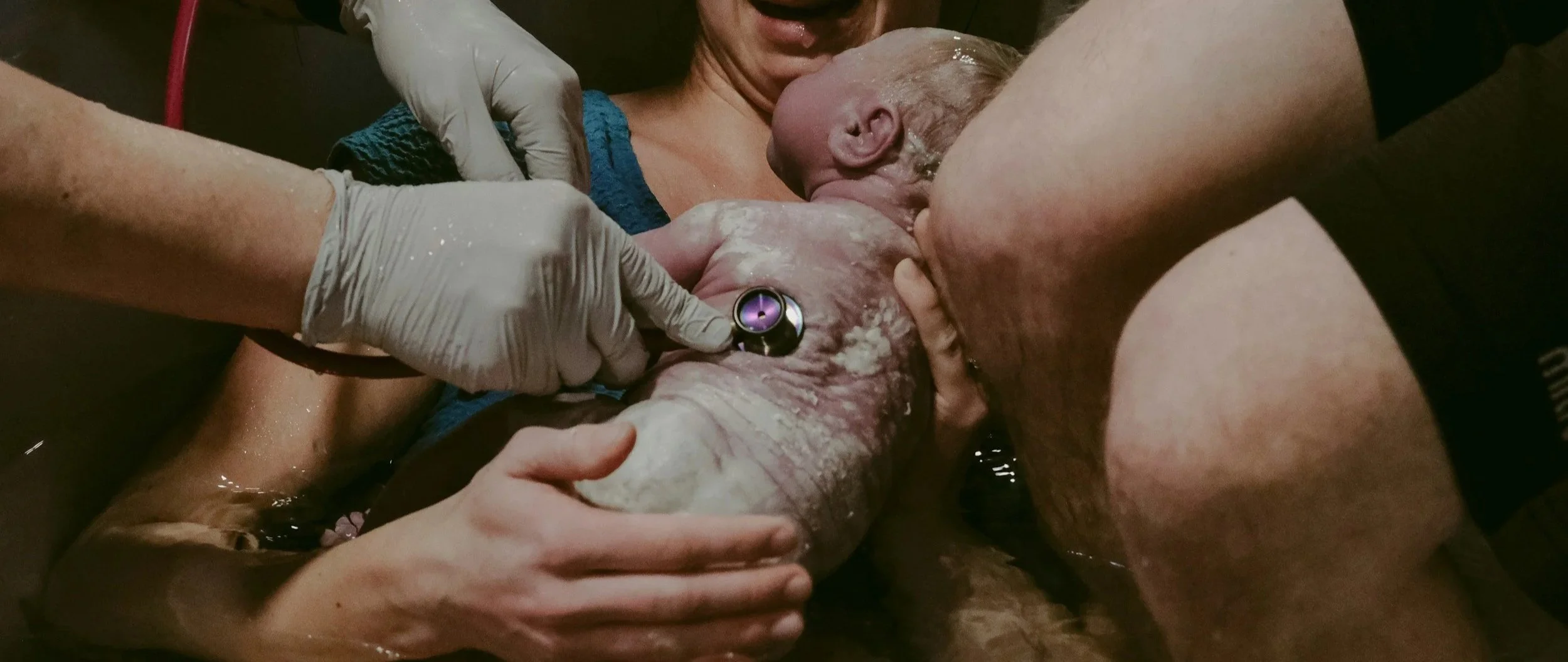 A woman giving birth in a home birth setting, surrounded by medical personnel assisting with the delivery supported by a doula and midwives