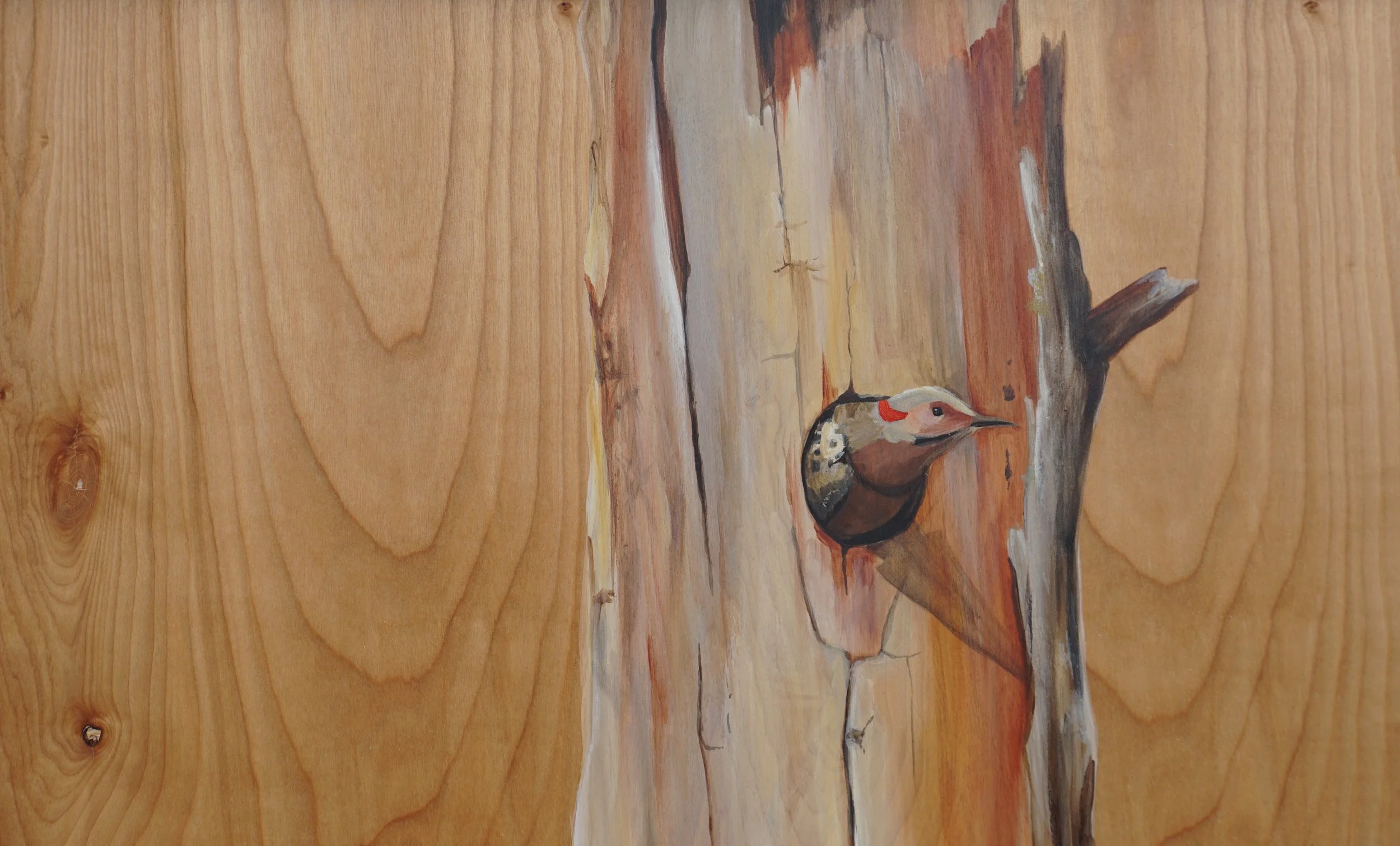 Painting of a woodpecker on a tree trunk on a wooden surface.