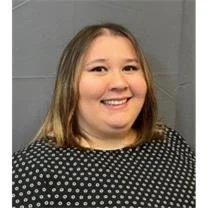 A woman with dark wavy hair and red lipstick laughing outdoors, wearing a red turtleneck.