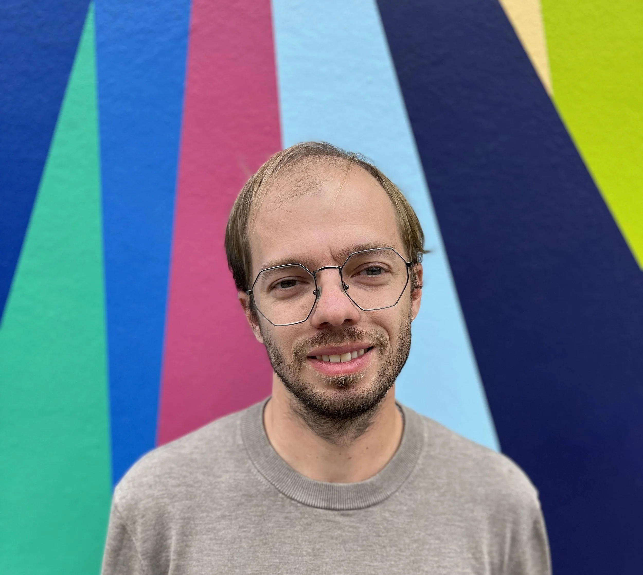 A woman with shoulder-length black hair smiling outdoors surrounded by green plants.