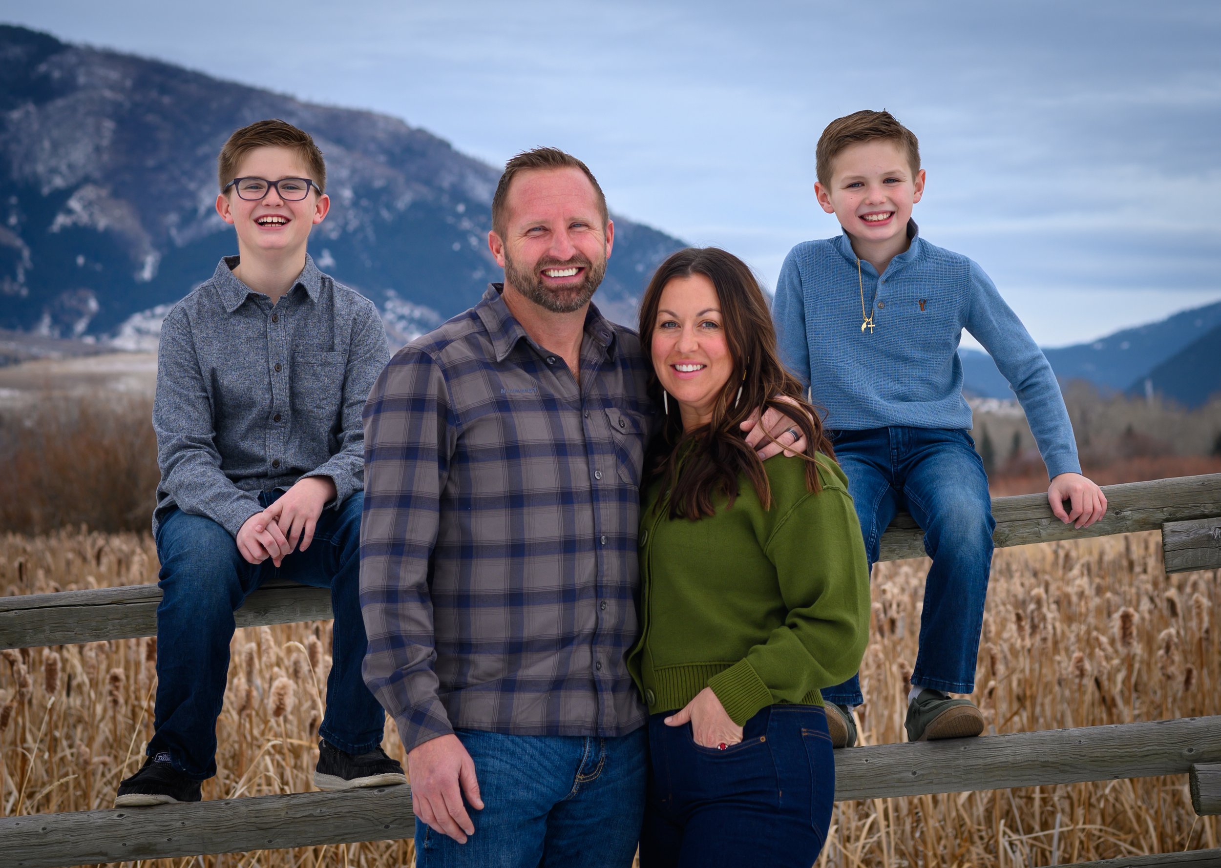 A family of six sitting in a wheat field, smiling at the camera.