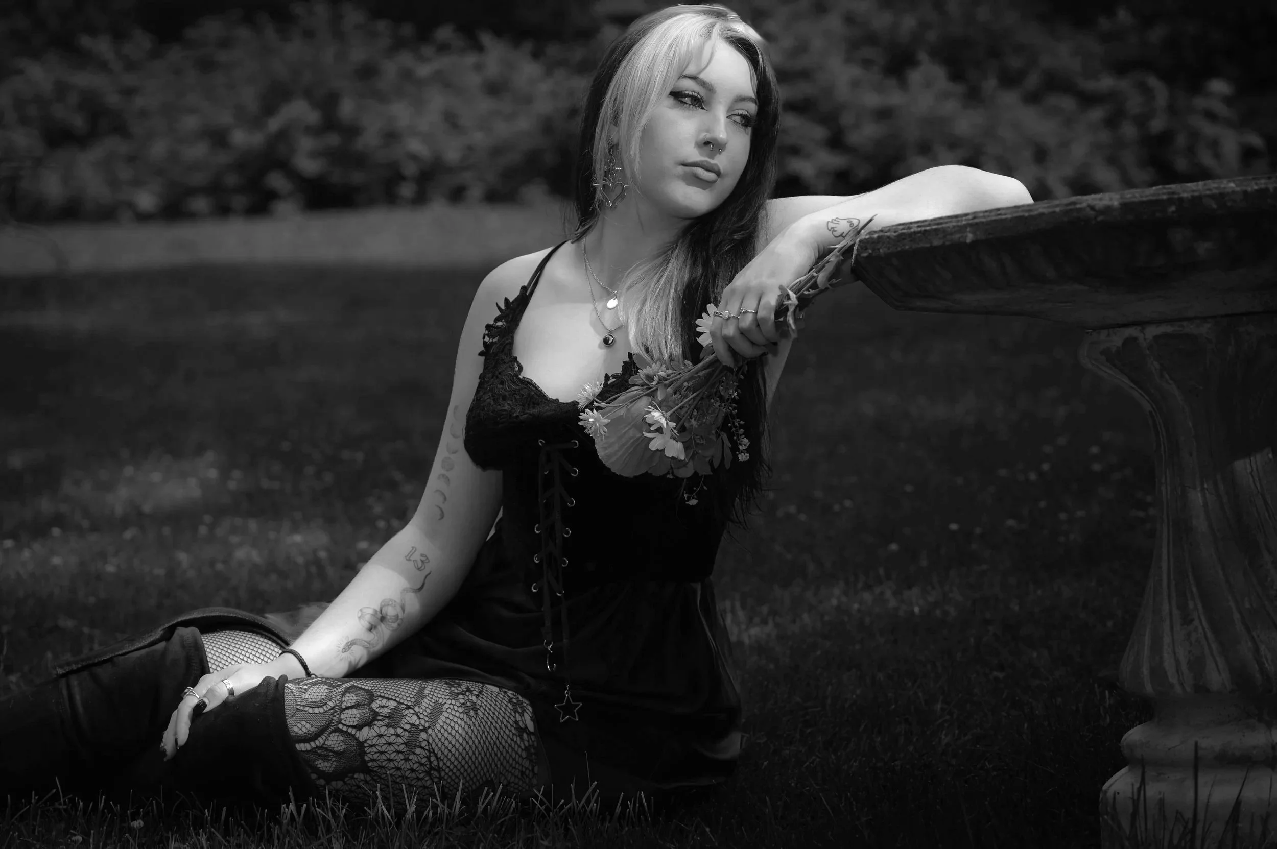 Black and white photo of a woman with closed eyes and relaxed expression, standing outdoors with sunlight filtering through trees in the background.