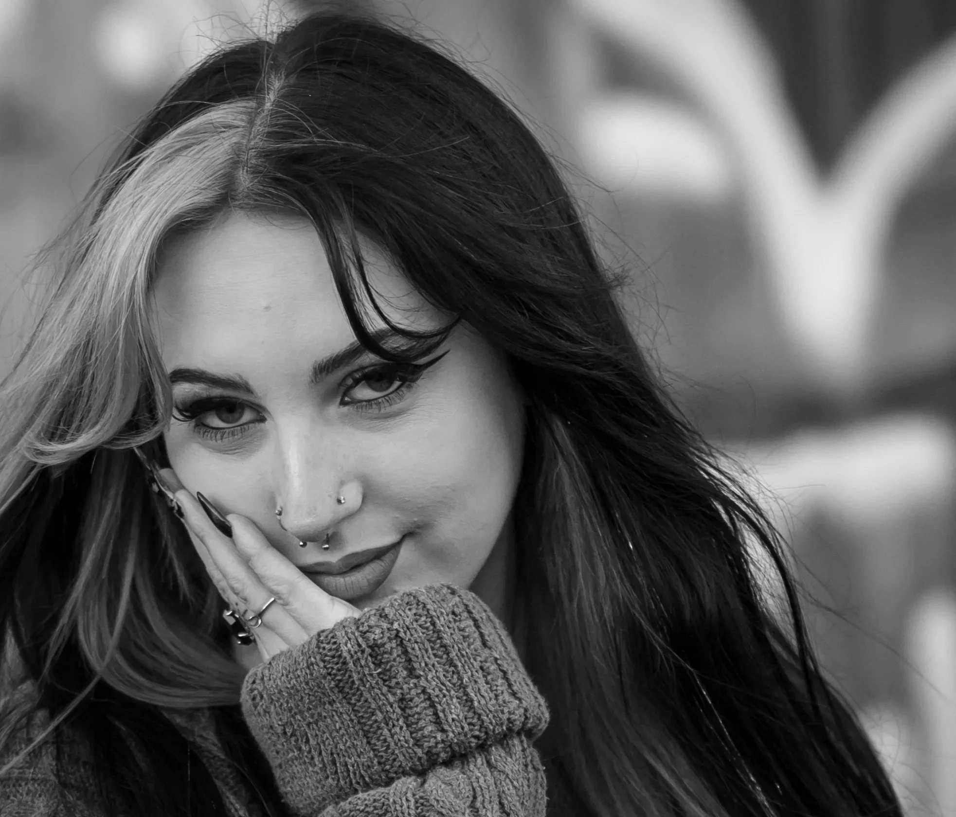 Black and white photo of a woman with closed eyes and relaxed expression, standing outdoors with sunlight filtering through trees in the background.