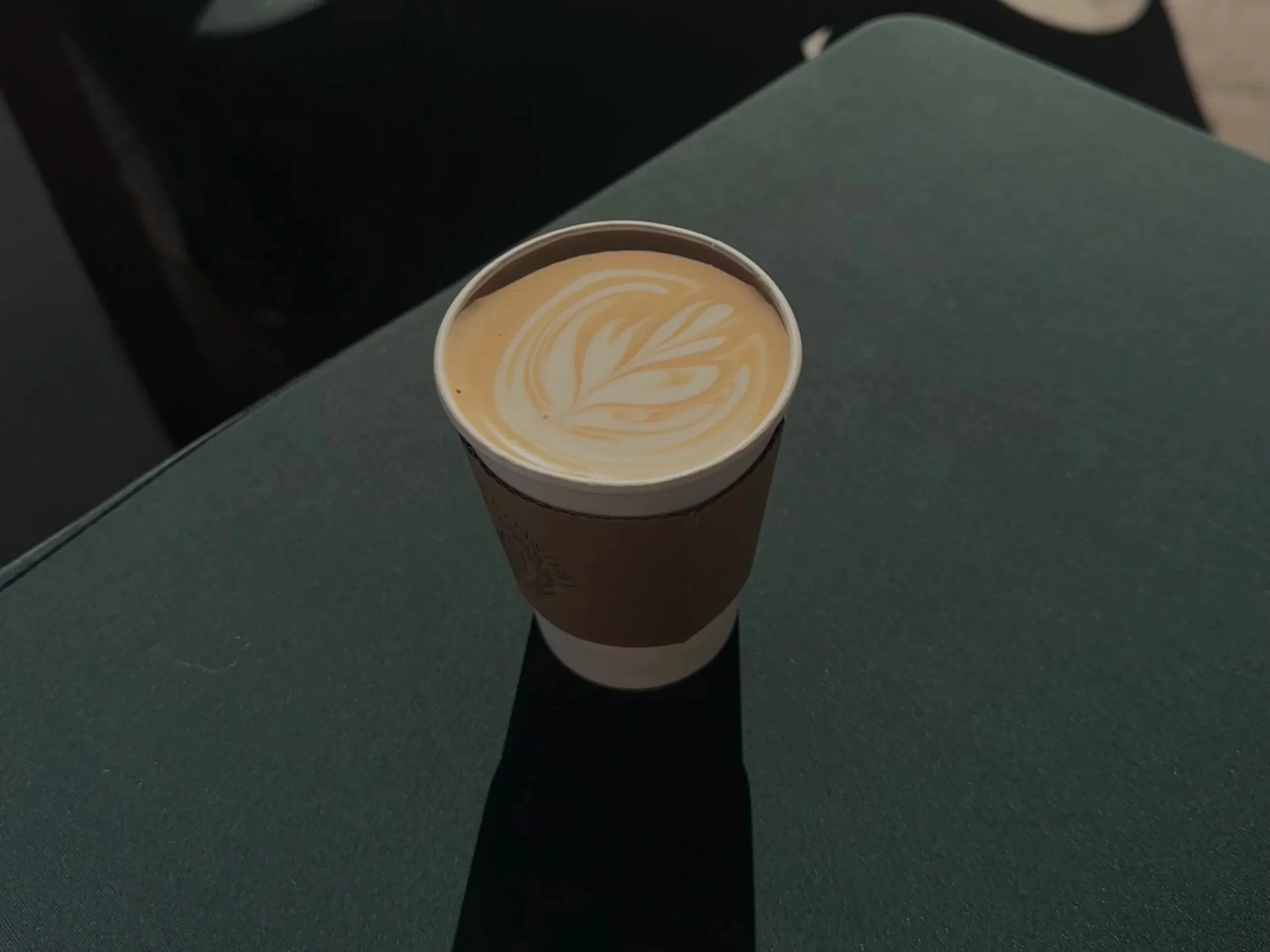 A cup of coffee with latte art sitting on a green table.