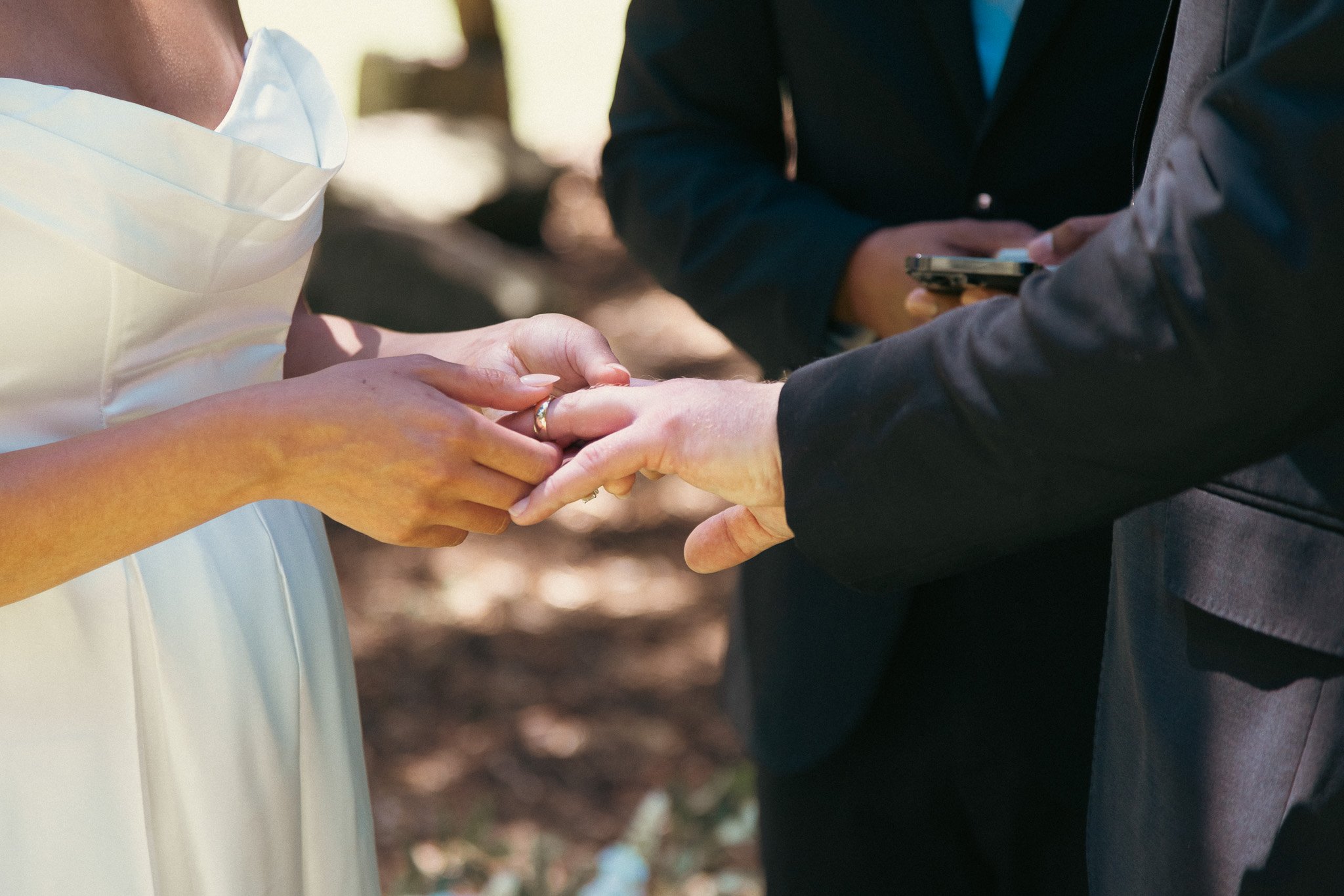 A couple getting married and exchanging rings outdoors, with a officiant present.
