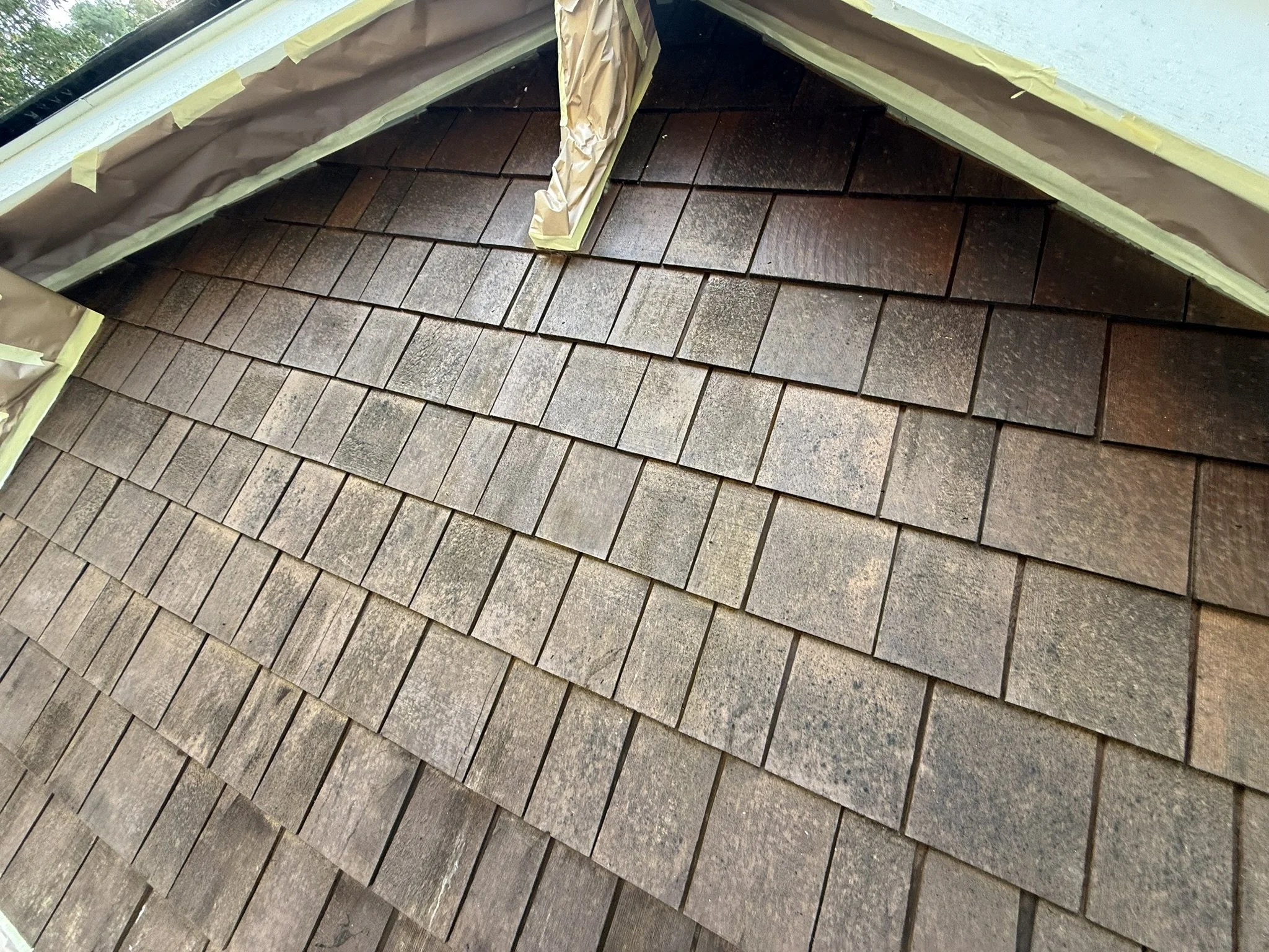 Close-up of a roof with newly installed brown shingles, and edges covered with masking paper and tape for protection during construction or repair.