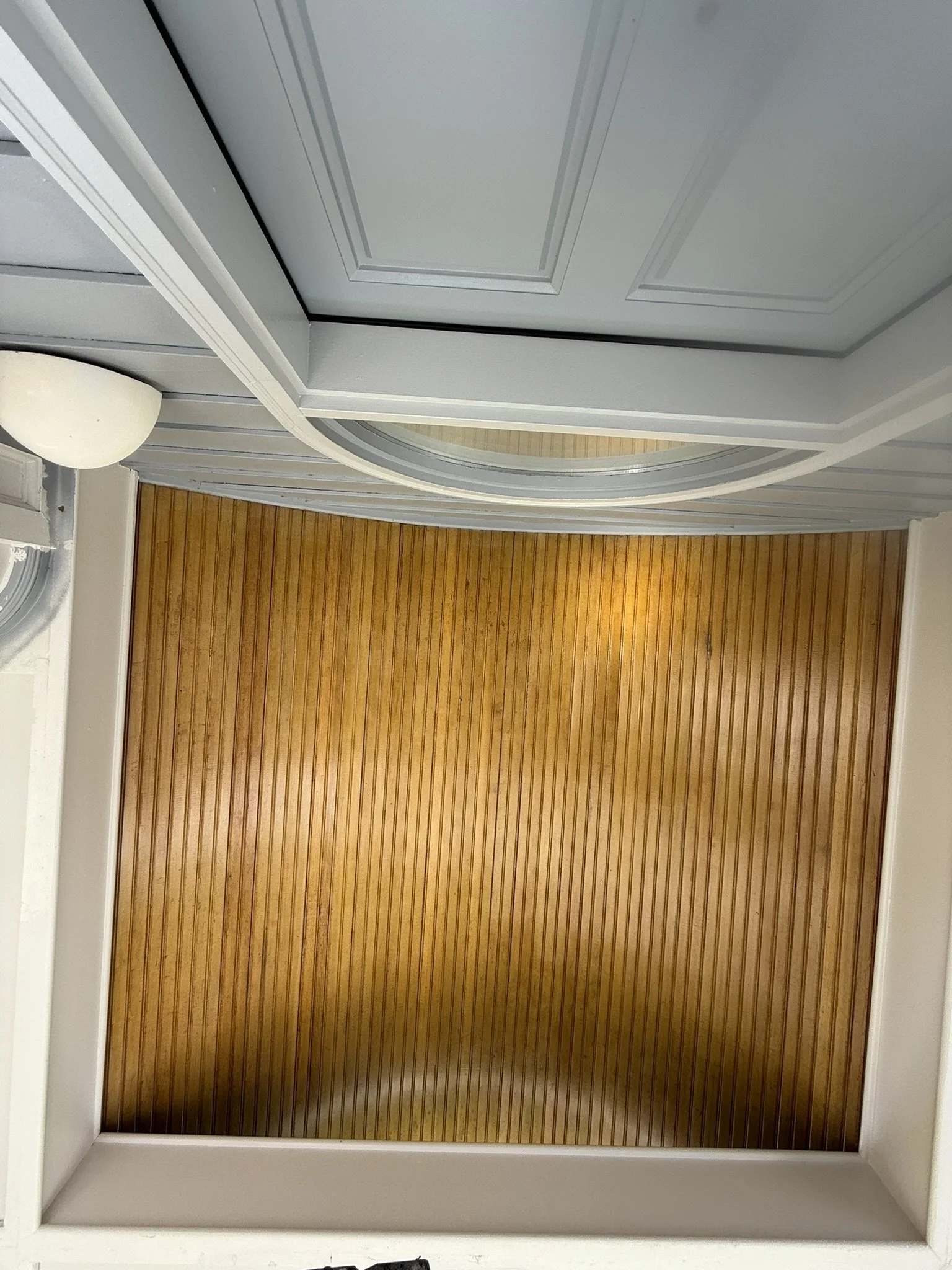 An interior view of a room with a wooden floor, white walls, and a gray ceiling with decorative molding.