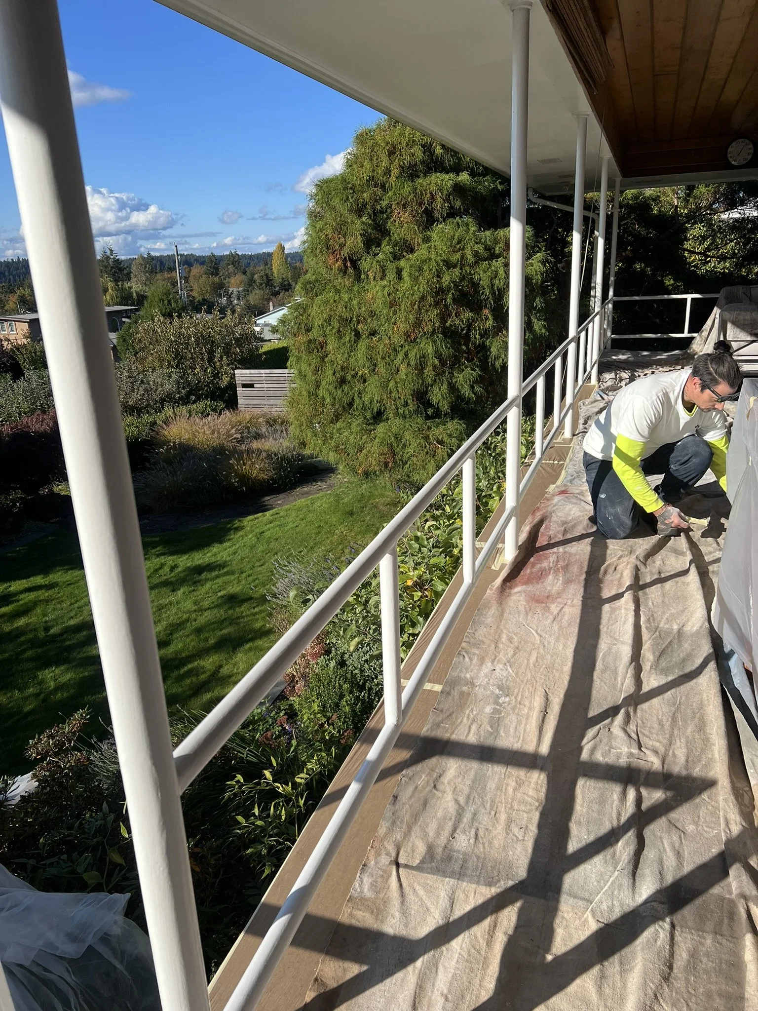 A person working on a balcony, with lush green trees and a clear blue sky in the background.