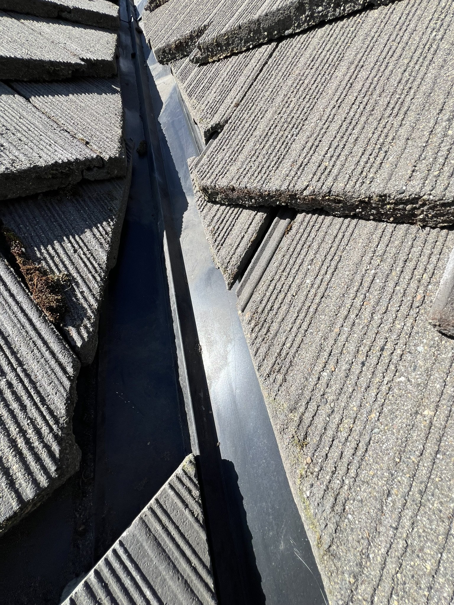 Close-up view of a roof with asphalt shingles and flashing in a ridge valley.