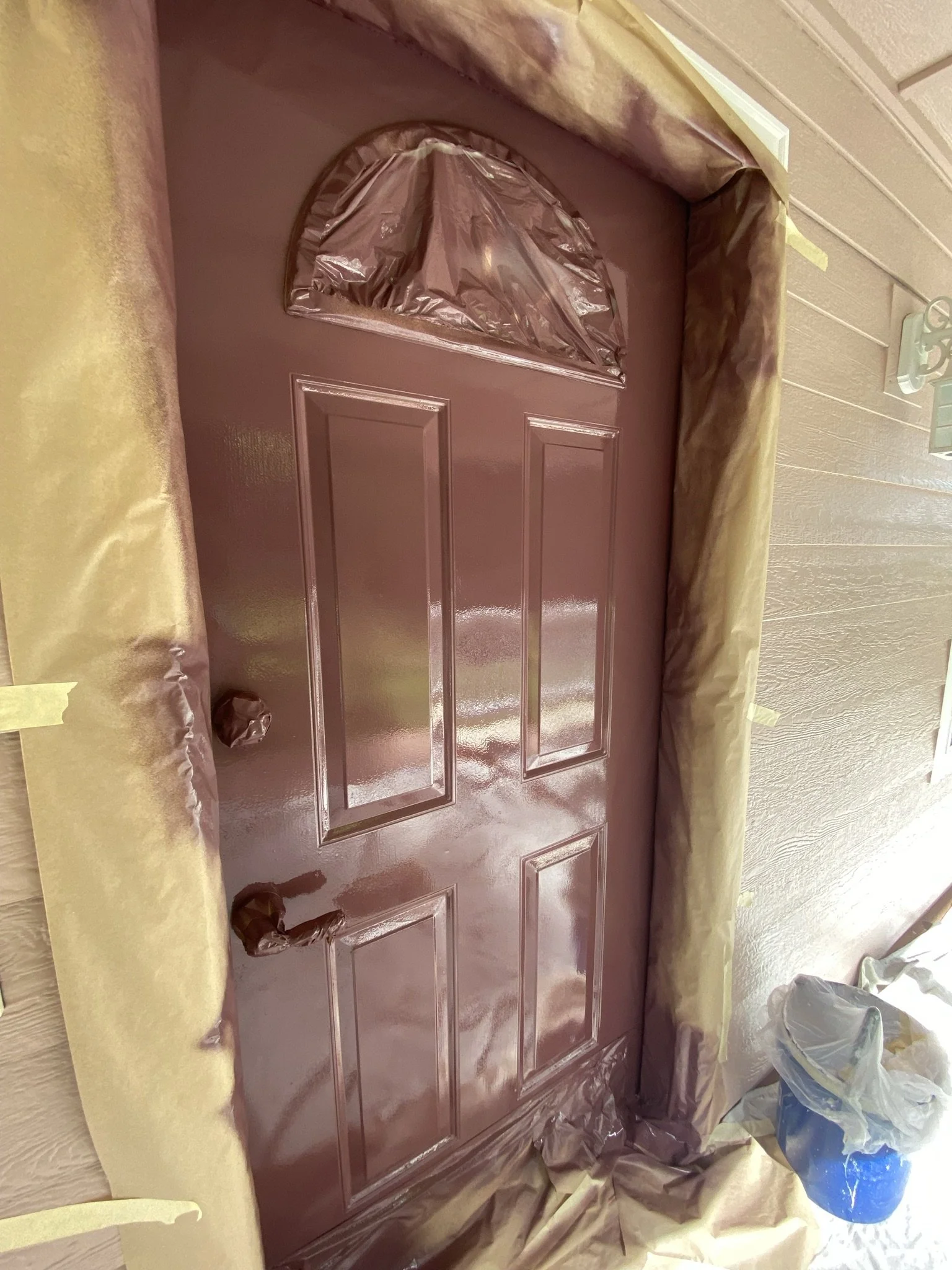 A door painted in a shiny mauve color, with brown painter's paper covering the surrounding wall and parts of the door frame for protection during painting.