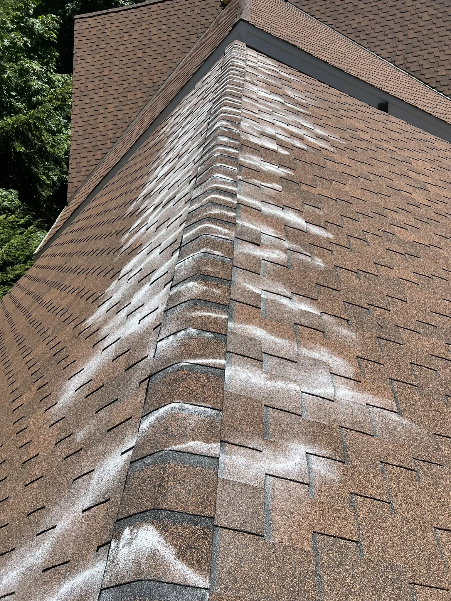 Close-up view of a brown shingled house roof with a prominent ridge line and some weathering or discoloration on the shingles.