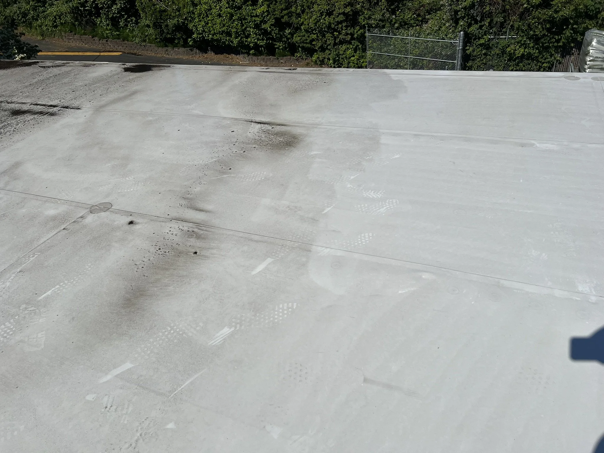 Flat rooftop with black soot marks and footprints, bordered by a fence and trees in the background.