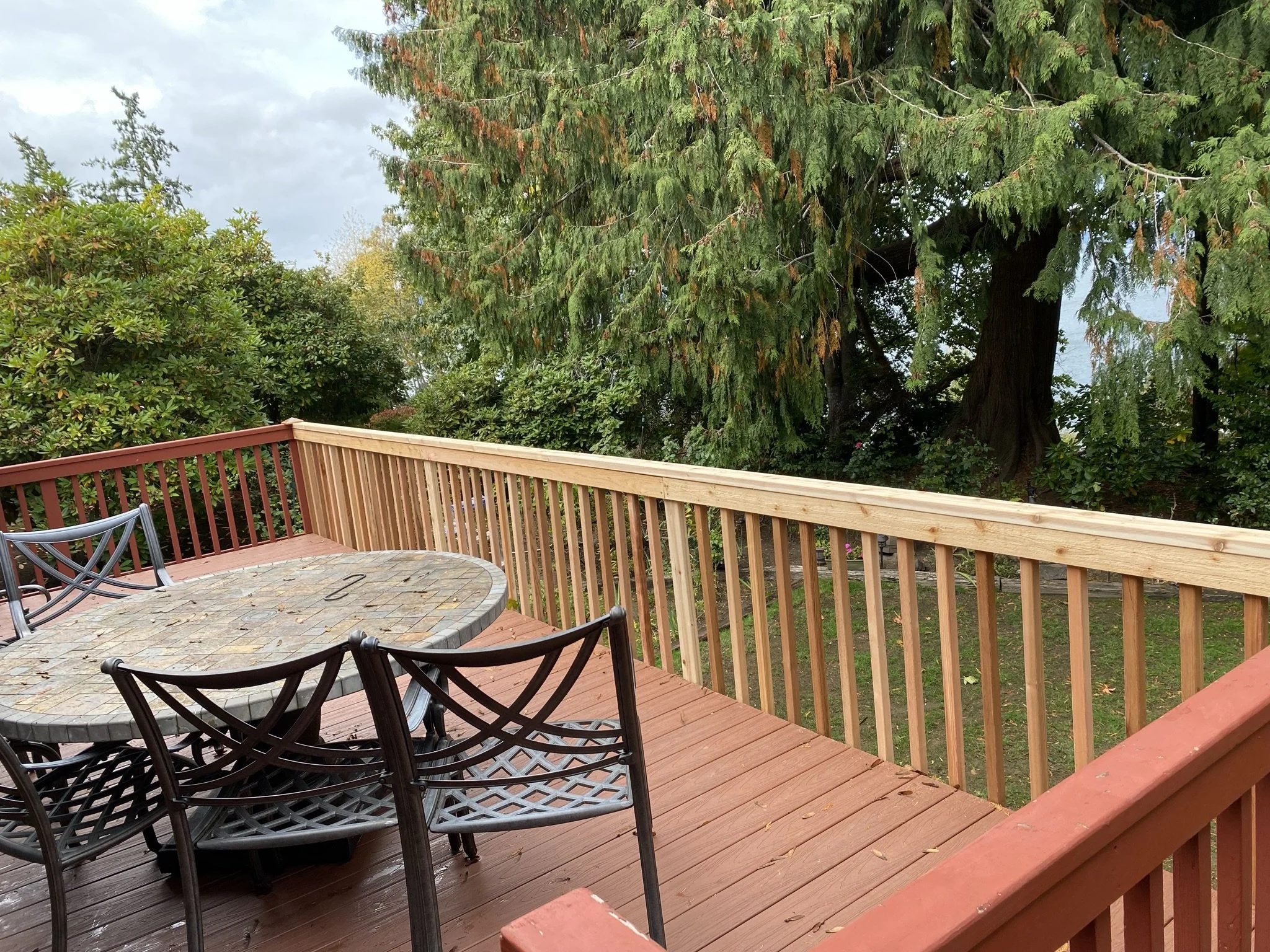A deck with a stone-top table and black metal chairs, surrounded by green trees and bushes.