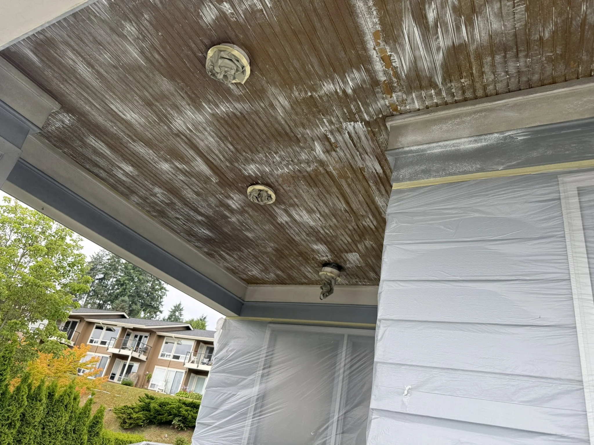 Undergoing exterior porch ceiling renovation, covered light fixtures with protective tape, and white plastic sheeting on walls.