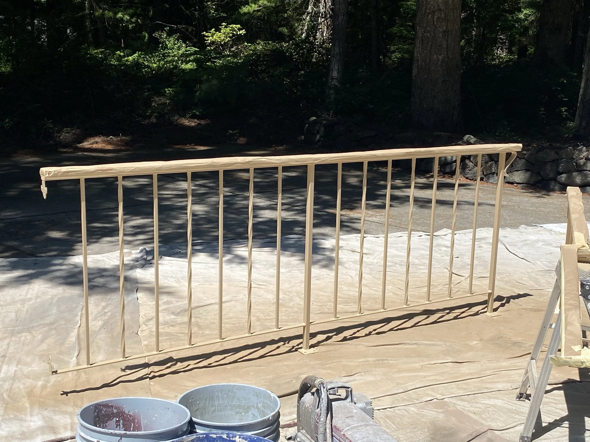 Unpainted metal railing standing on a tarp, outdoors with trees and rocks in the background.