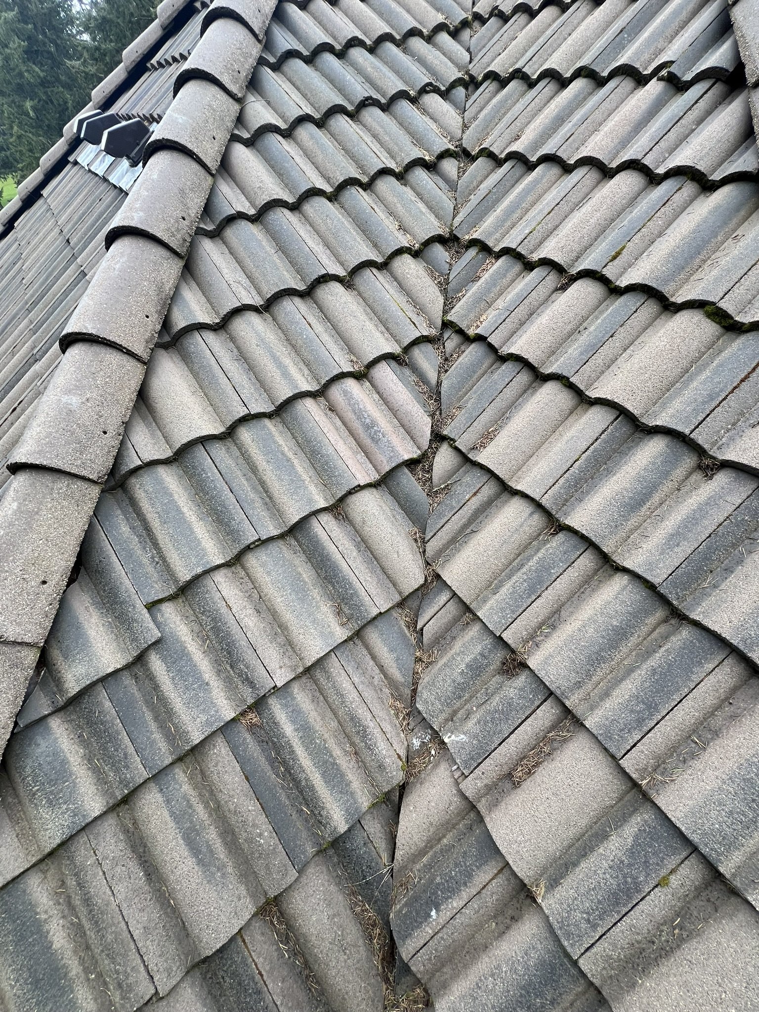 Close-up of a roof with gray, weathered ceramic tiles, some with moss and dirt, arranged in overlapping rows.