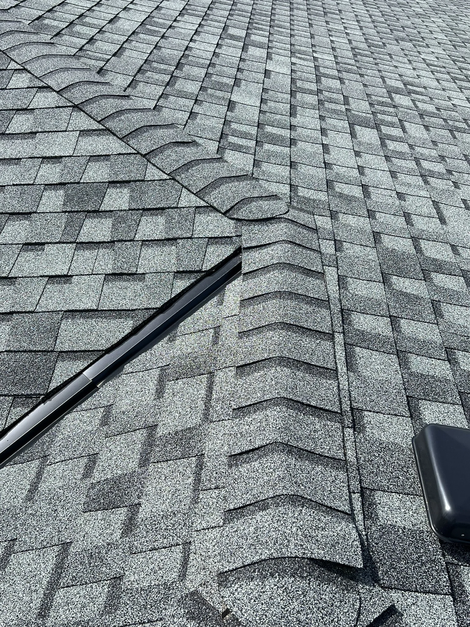 Close-up of a shingled roof with a vent pipe and a solar-powered vent or alarm.