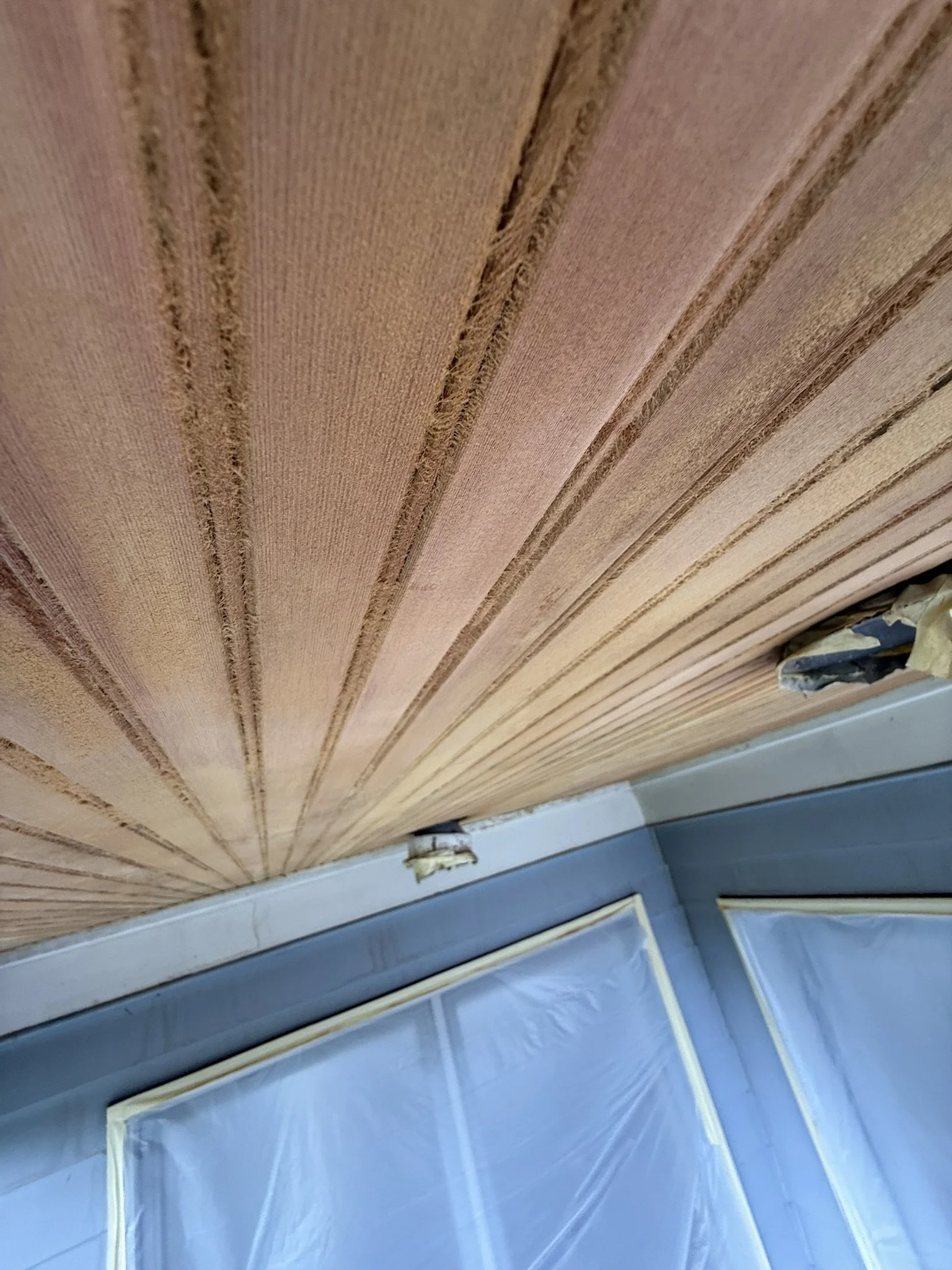 Close-up view of a textured ceiling with wood paneling and a corner of a wall covered in protective plastic during renovation.