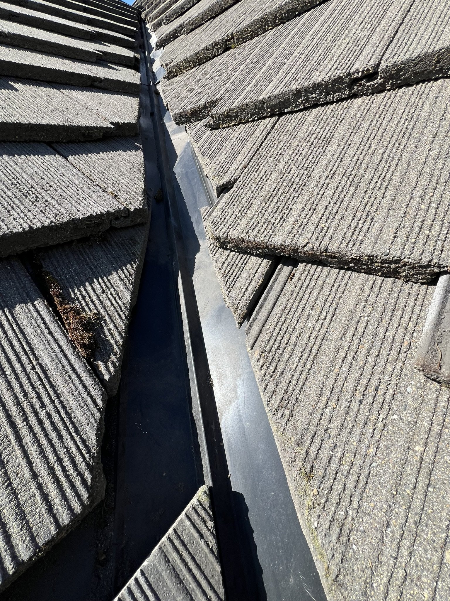Close-up of a roof's ridge with split shingles and a metal flashing installed in the gap.