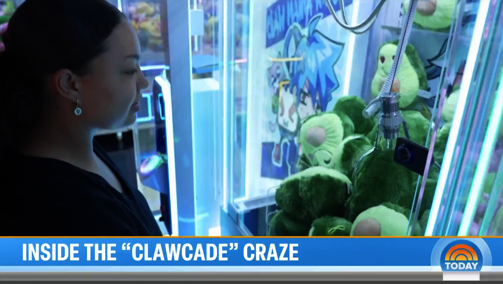A woman is standing in front of a claw machine filled with green plush toys, viewing the toys inside the machine.
