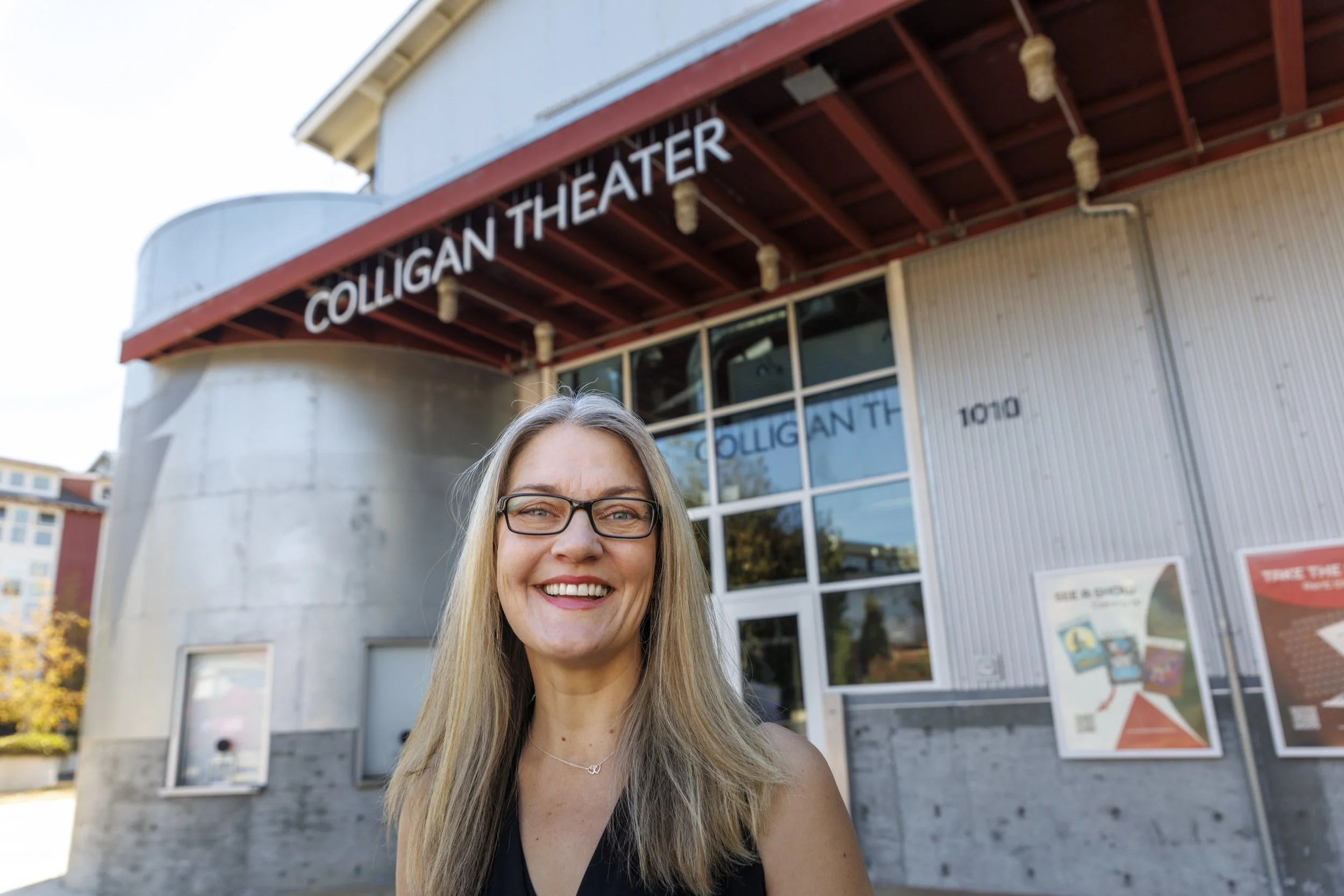 Lindsey Chester smiling outside the Colligan Theater, a modern building with large windows and a sign reading 'Colligan Theater' above the entrance.
