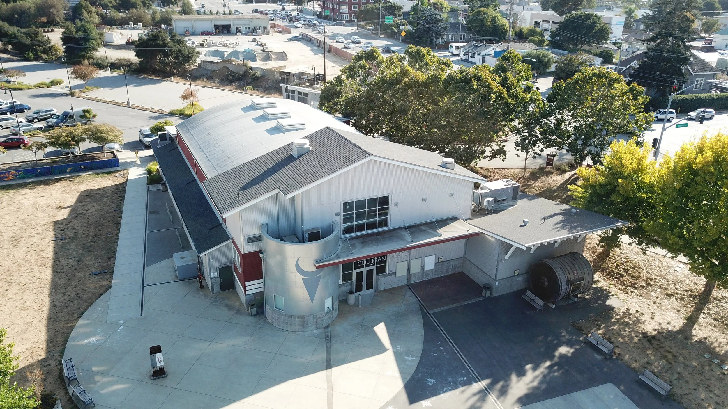 Aerial view of a small theater building with a rounded front entrance and a large marquee, surrounded by a parking lot, trees, and nearby streets.