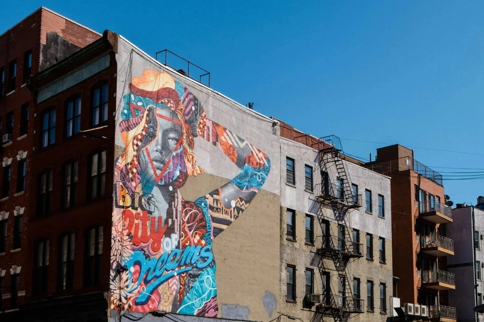 Colorful mural of a woman with braided hair and big earrings on the side of a building, with the words 'Big City of Dreams'.