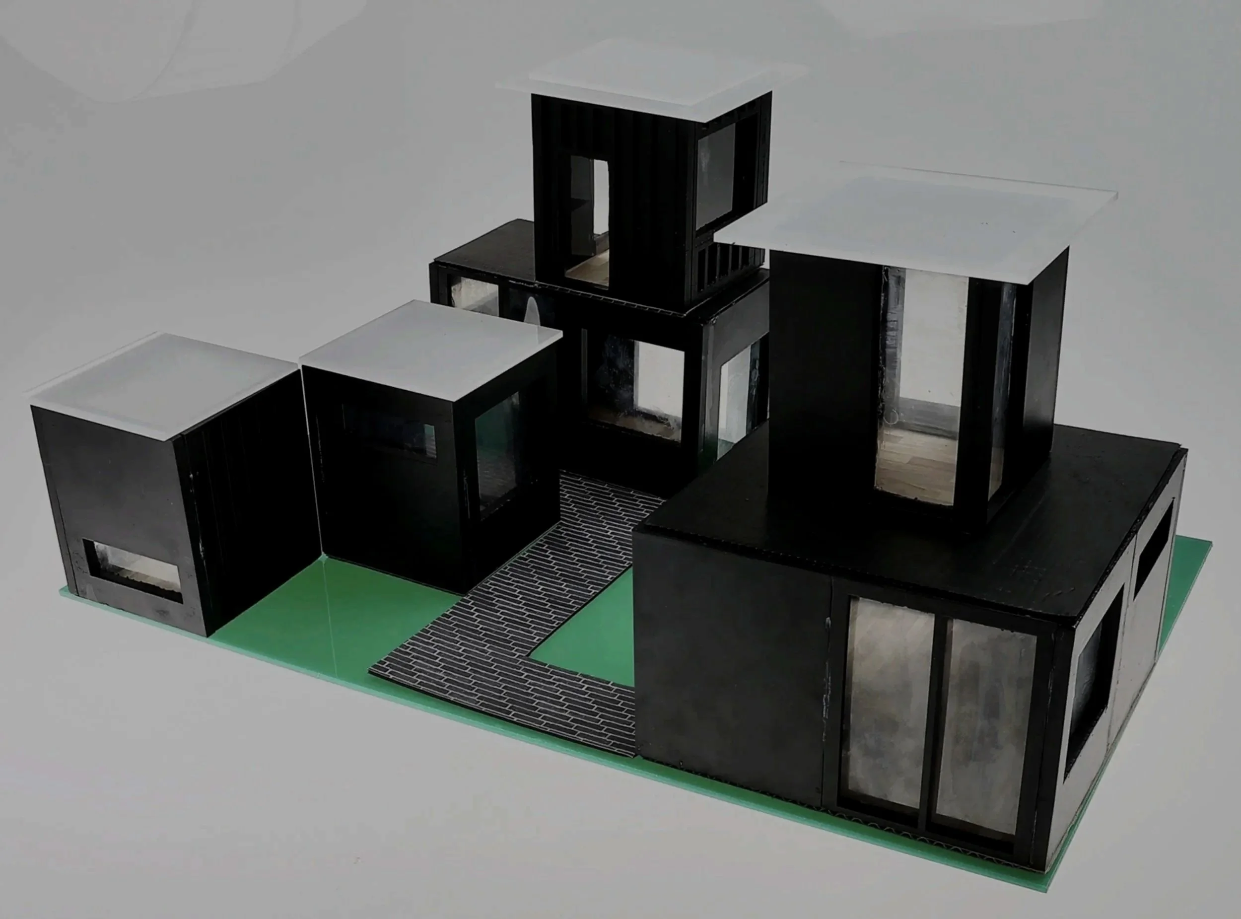 A scale model of a modern, multi-level house with black walls and large windows, set on a green and patterned base.