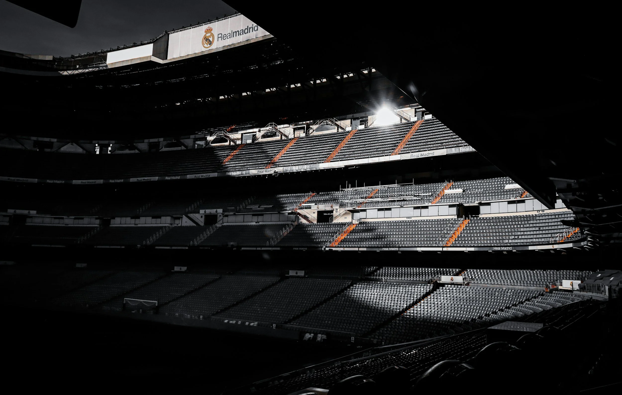Empty stadium with sunlight shining through, Real Madrid banners, and seating sections visible.