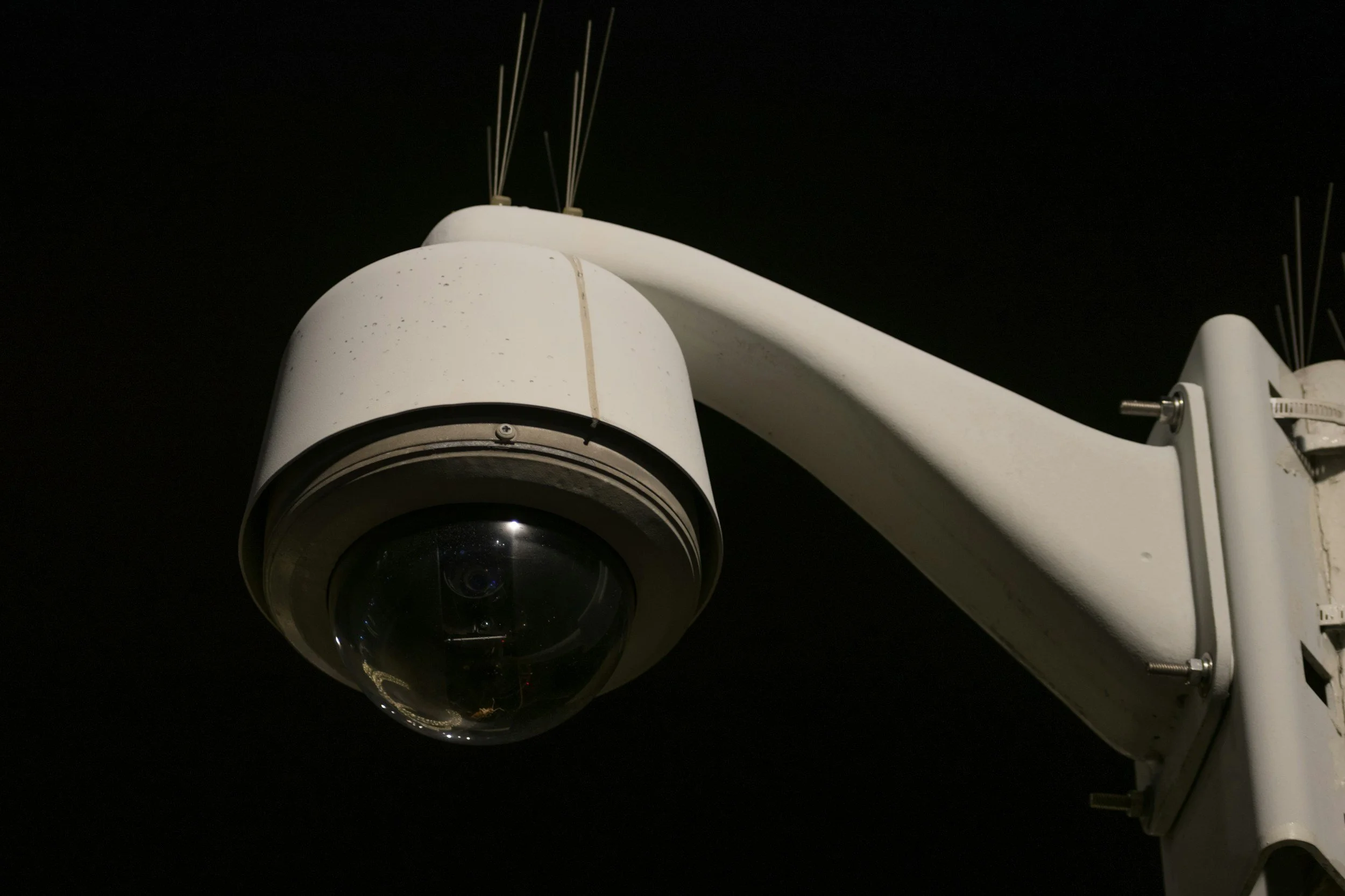 Close-up of a white security camera mounted on a white arm against a dark night sky.