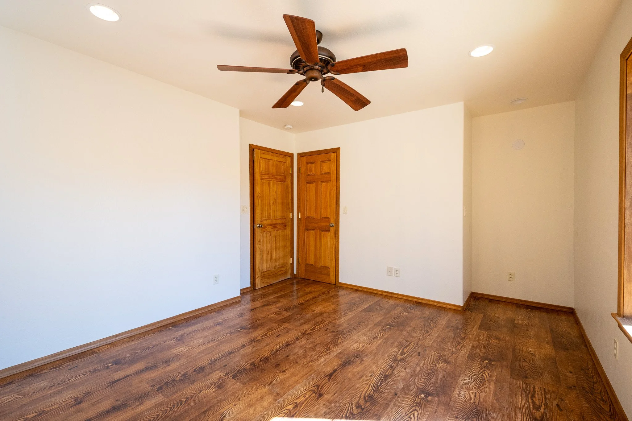 Empty room with wooden floors, white walls, two closed wooden doors, and a ceiling fan.