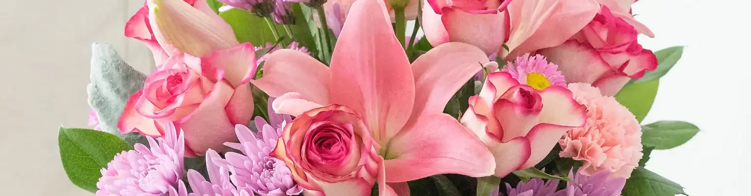 A bouquet of pink lilies, roses, and other pink and purple flowers with green leaves.