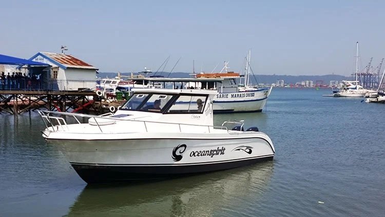A white boat with the brand name 'oceanspirit' on the side, docked in a harbor with other boats and a wooden pier in the background.