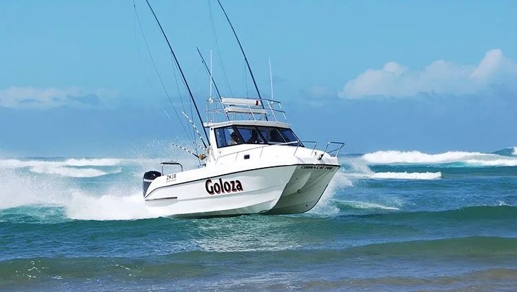 A white fishing boat named Goloza speeding over the ocean waves on a sunny day.