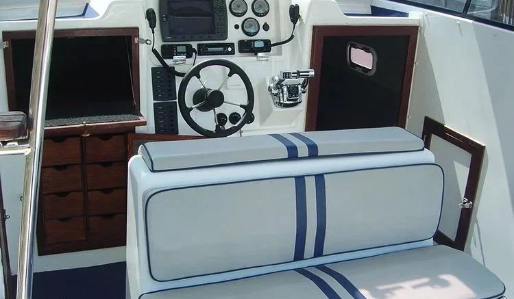Boat cabin interior with a white bench seat and a control panel with navigation equipment.